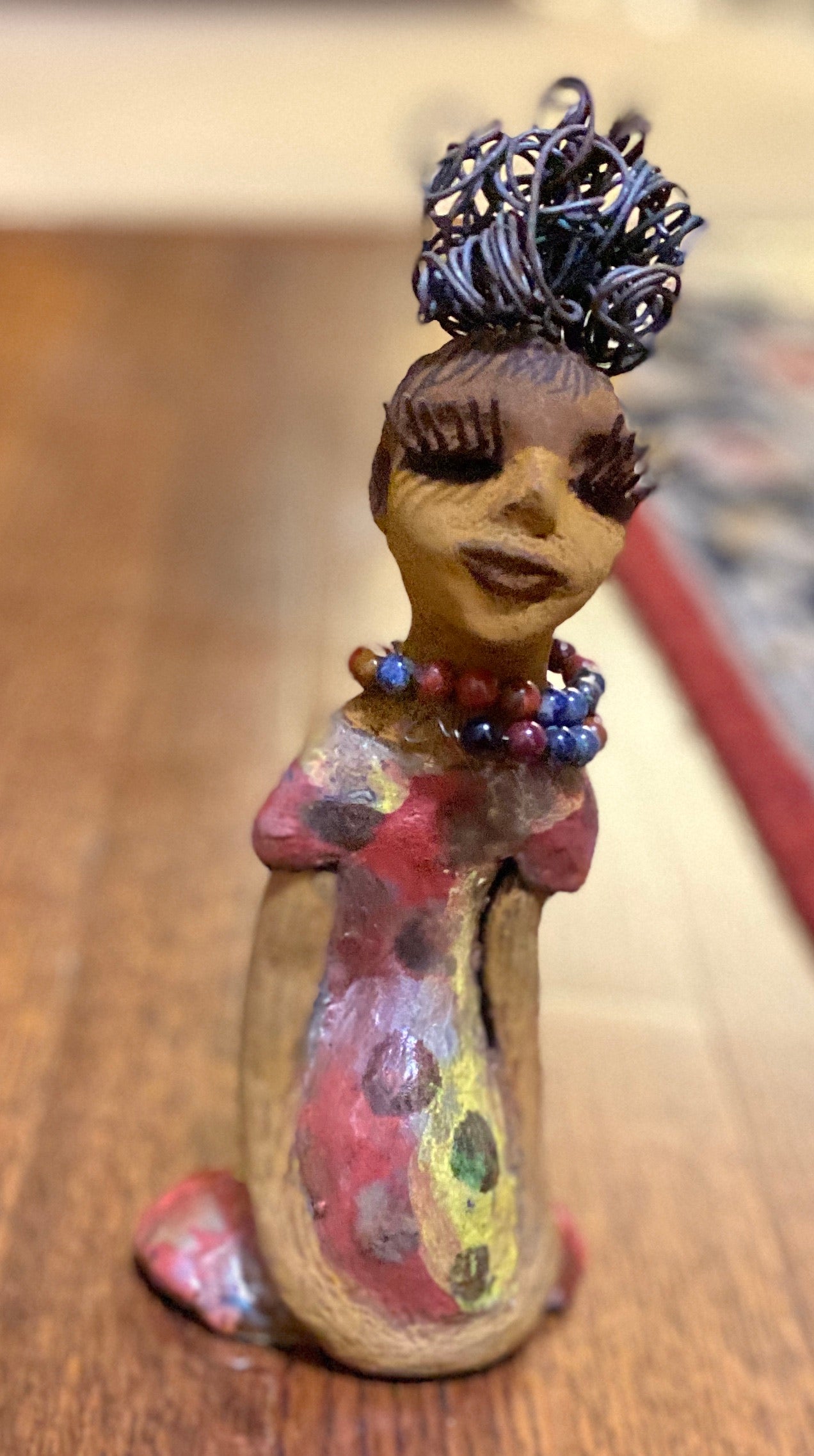 You know someone like Tiffanie. One who reaps elegance and sophistication!  Tiffanie stands 9”x 4" x 4" and weighs 1.03 lbs.  She has a two tone light beige complexion with 2 feet of 16 gauge spiral coiled wire hair.  Tiffanie metallic copper red and yellow  dress is accented by a multicolored beaded necklace. Tiffanie’s long lashes and  black eye shadow gives her a distinguished mystical look.