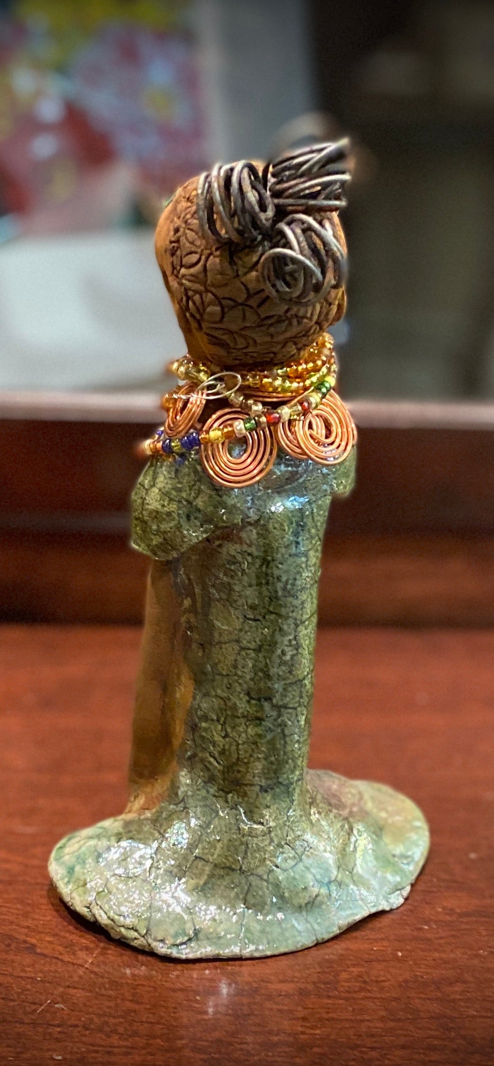 Kaleesia stands 9” x 5" x 2.5" and weighs 1.03 lbs. She has a lovely beige brown complexion with short etched braided clay hair. Kaleesia long loving arms rest beside her multicolored copper green dress. Kaleesia is a sophisticated lady that will grace your home.