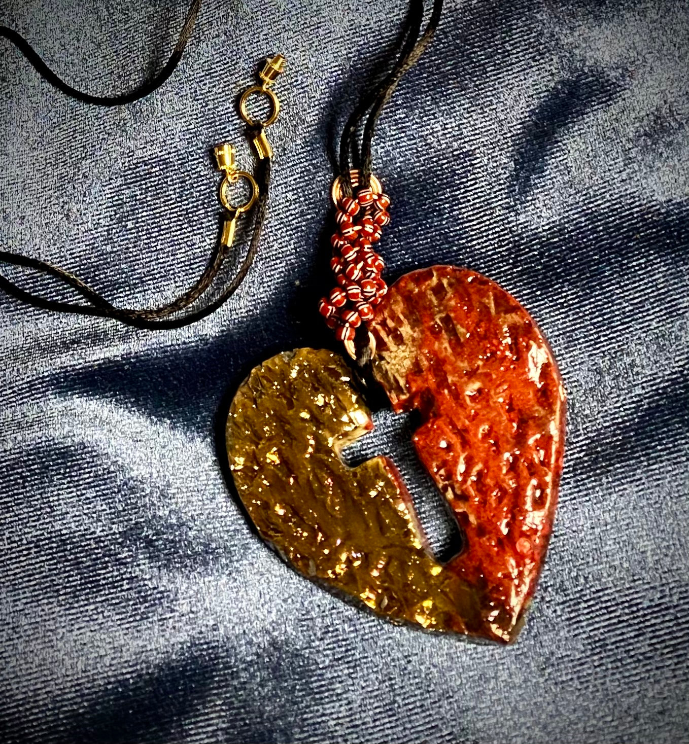 Have A Heart ! Each heart pendant is handmade with love! It is 3"x 3" and weighs approx. 3ozs. This pendant has a red and gold metallic raku glazes that renders a unique translucent patina. The heart is textured and has a cut out cross in the center. It holds a spiral of red and white mini beads on a spiral copper wire. This pendant has a nice 12" black suede cord!