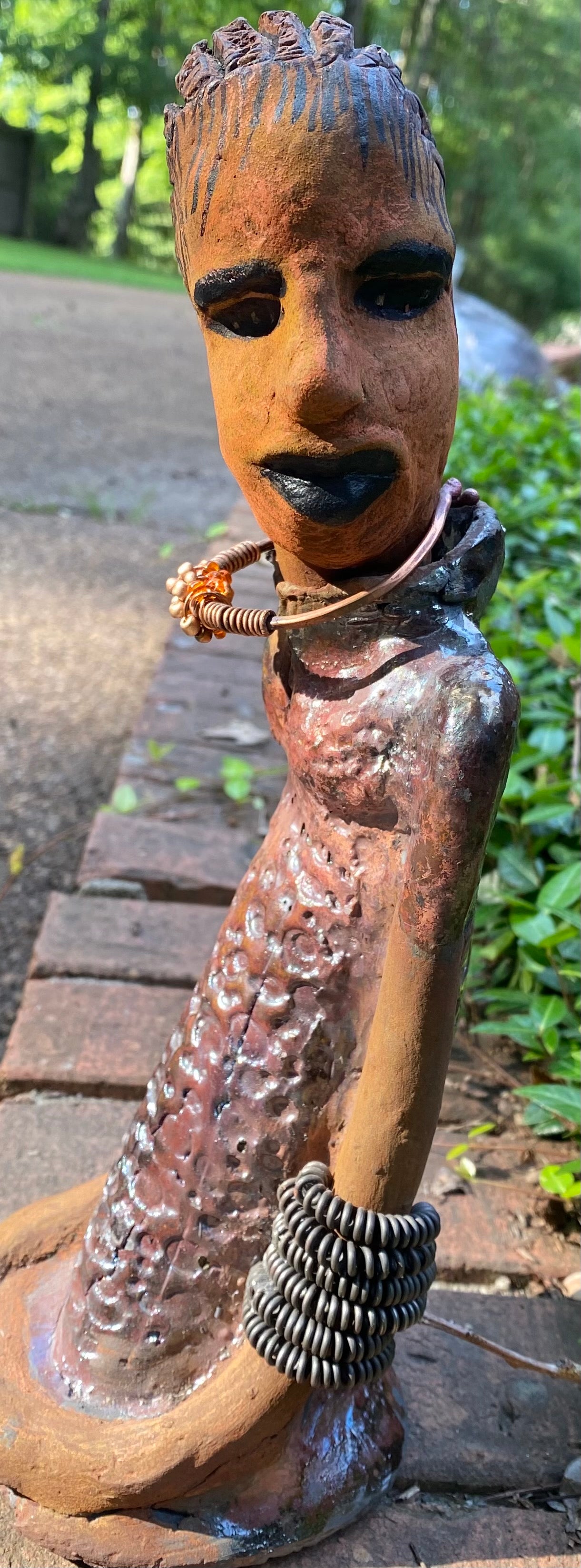 Jessie says no to wire hair and yes to the braids. Jessie stands 12" x 5" x 4.5" and weighs 1.03 lbs. She has a lovely honey brown complexion.  Jessie long loving arms rest beside her alligator copper green dress. She wears a strand of amber beads with spiral copper that can be worn as a bracelet. Jessie is a sophisticated lady that will grace your home.