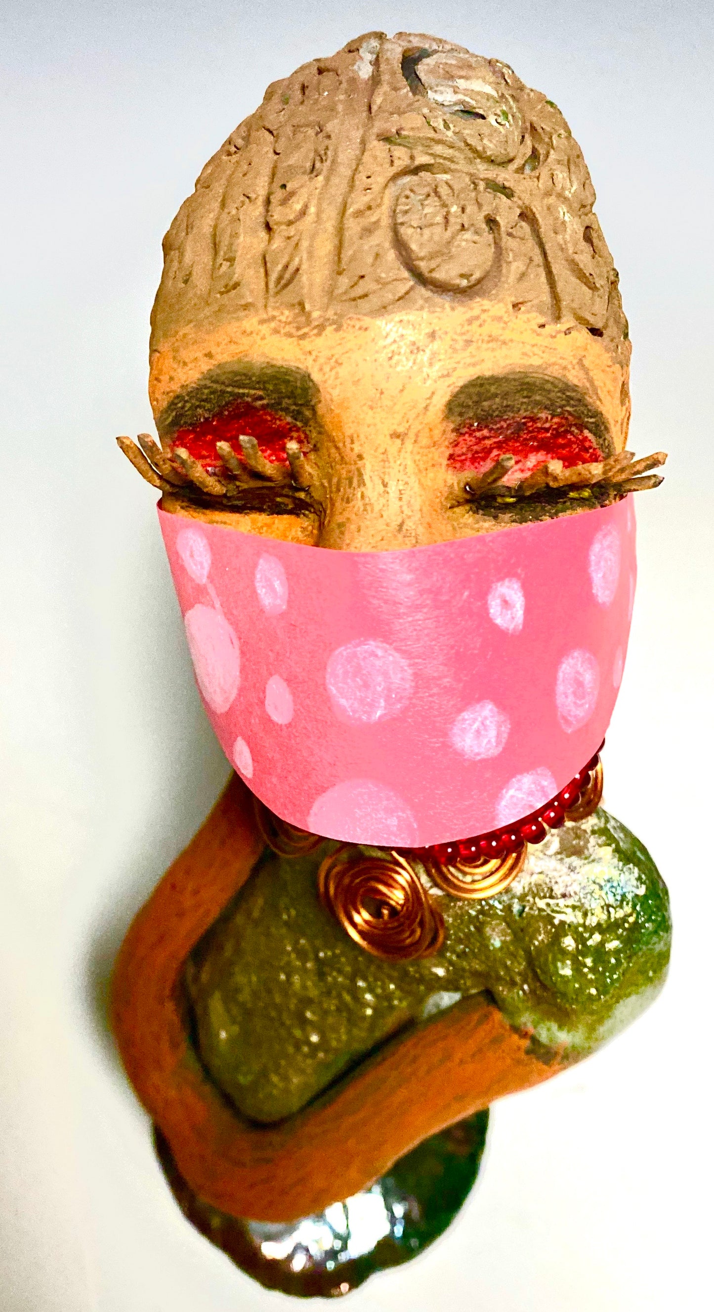 Meet Mona! Mona stands 11.5" x 4" x 4" and weighs 1.81 lbs. She has a lovely chocolate brown complexion with chocolate brown lips. She has a braided hairstyle. Mona has a colorful metallic antique copper glazed dress. She wears a spiral copper wire necklaces on top of a beaded ruby red collar. With long lashes and eyes wide opened, Mona has hopes of finding a new home. You may have noticed, Mona is the one of a few herdew sculptures that wears a face mask during this unprecedented time.