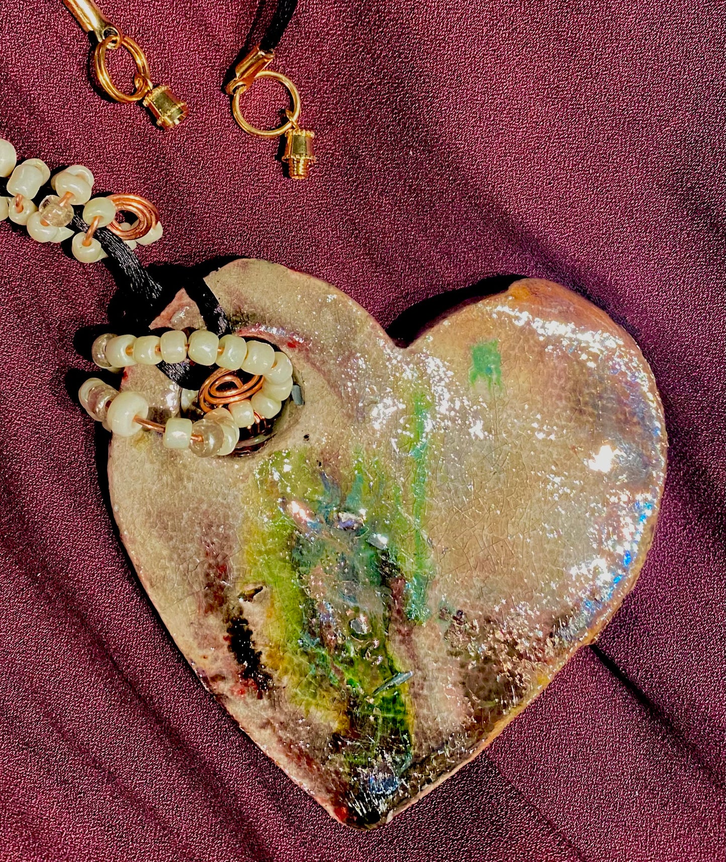 Have A Heart! Each heart pendant is handmade with love! It is 3"x 3" and weighs approx. 3ozs. This pendant has a copper gold metallic raku glazes that renders a unique translucent patina. The heart has a textured pattern . It holds a spiral of white mini beads on a spiral copper wire. This pendant has a nice 12"black rattail cord!