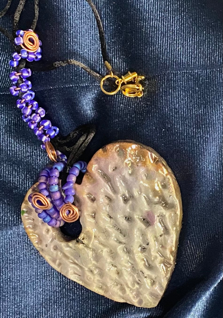 Have A Heart ! Each heart pendant is handmade with love! It is 3"x 3" and weighs approx. 3ozs. This pendant has a white metallic raku glazes that renders a unique translucent patina. The heart has a textured pattern . It holds a spiral of blue mini beads on a spiral copper wire. This pendant has a nice 12" black suede cord!