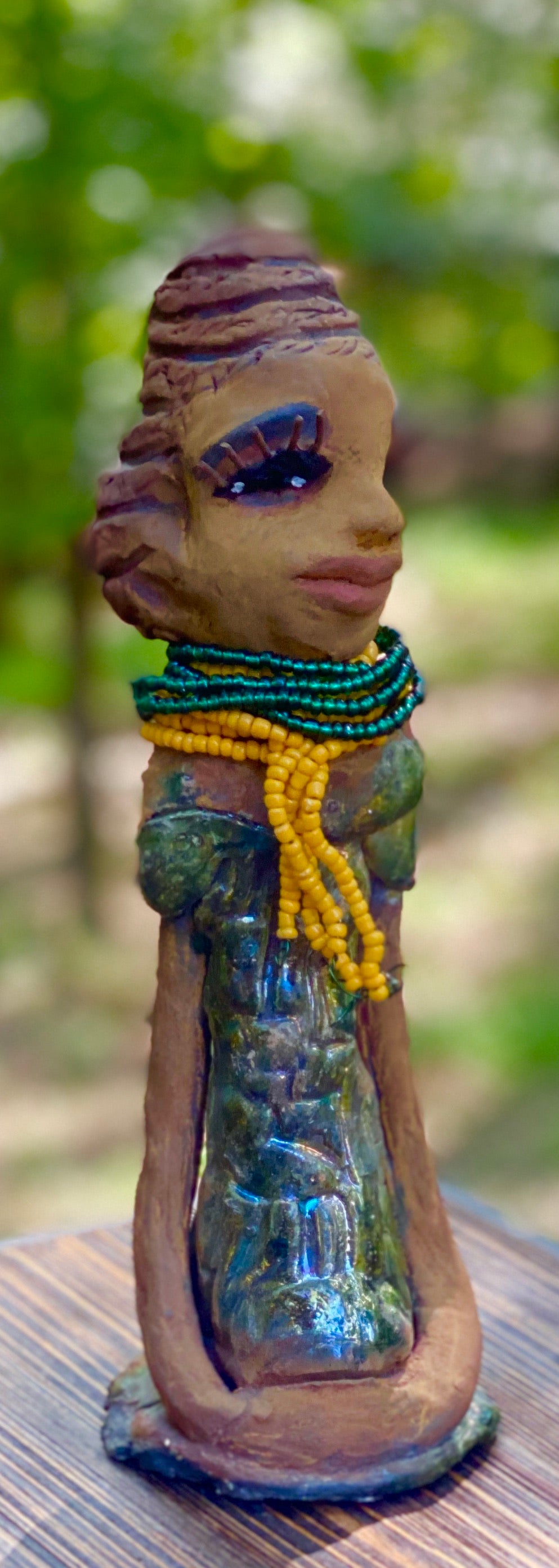 Meet Jazmyne! Jazmyne stands 11" x 4" x 4" and weighs 2.5 lbs. She has a lovely honey brown complexion with  reddish brown lips. She has a braided hairstyle.  Jazmyne has a colorful metallic green antique copper glazed dress. She wears a bright yellow beaded necklace. With long lashes and eyes wide opened, Jazmyne has hopes of finding a new home.    Jazmyne  will attract and spark conversation with guest in your home!