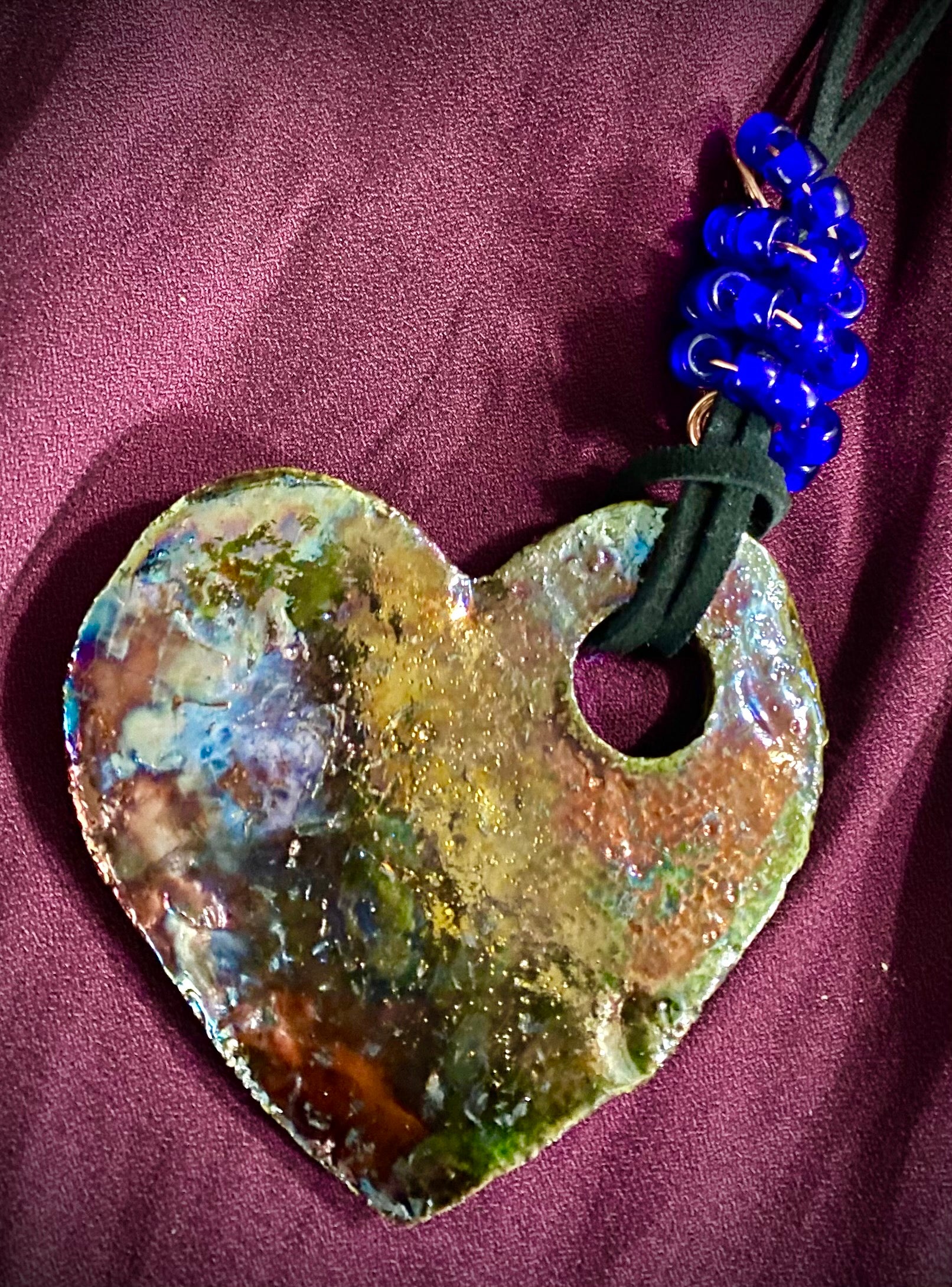 Have A Heart ! Each heart pendant is handmade with love! It is 3"x 3" and weighs approx. 3ozs. This pendant has a toasty copper metallic raku glazes that renders a unique translucent patina. The heart has a textured pattern . Both sides are  are different and equally beautiful! It holds a spiral of red violet mini beads on a spiral copper wire. This pendant has a nice 12"  black suede cord!