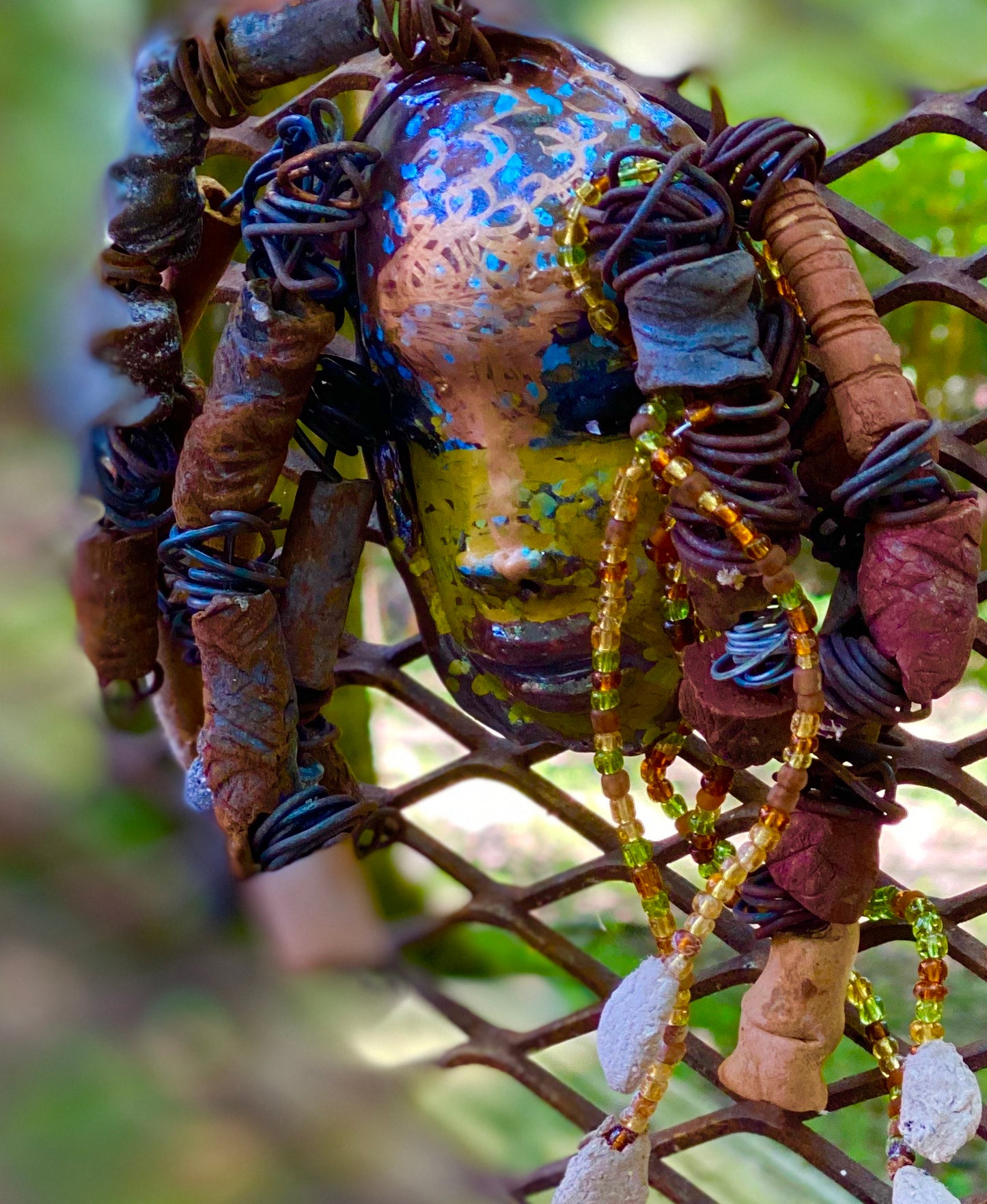 I started making mask soon after seeing authentic African artwork at the Smithsonian Museum of African Art. I was in total awe. Marali means she who listen was inspired by my visit there. Marali has a two tone metallic blue copper gold complexion. She is 7" x 5" and weighs 14 ozs. Marali has over 20 handmade raku fired beads. She has over 50 mini amber bead twisted as hair. Marali has over 6 feet of copper coiled 16 gauge wire hair.