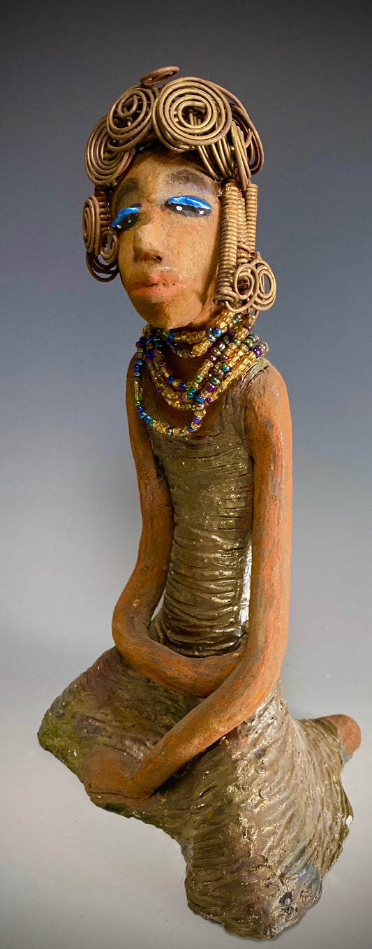 Meet Gloria! Gloria stands 12" x 7" x 5" and weighs 2.1 lbs. She has a lovely brown complexion. Her hair is gold and black. It took over 3 hours and 40 feet of coils and spirals of 16 gauge wire to complete! Gloria' coiled bangs hangs close to her slightly opened eyes. Wearing blue eye shadow, she has a multi colored dress with bright copper flashes to match. A string of iridescent amber colored beads surrounds her neck. With anticipation, Gloria wants to be with you.