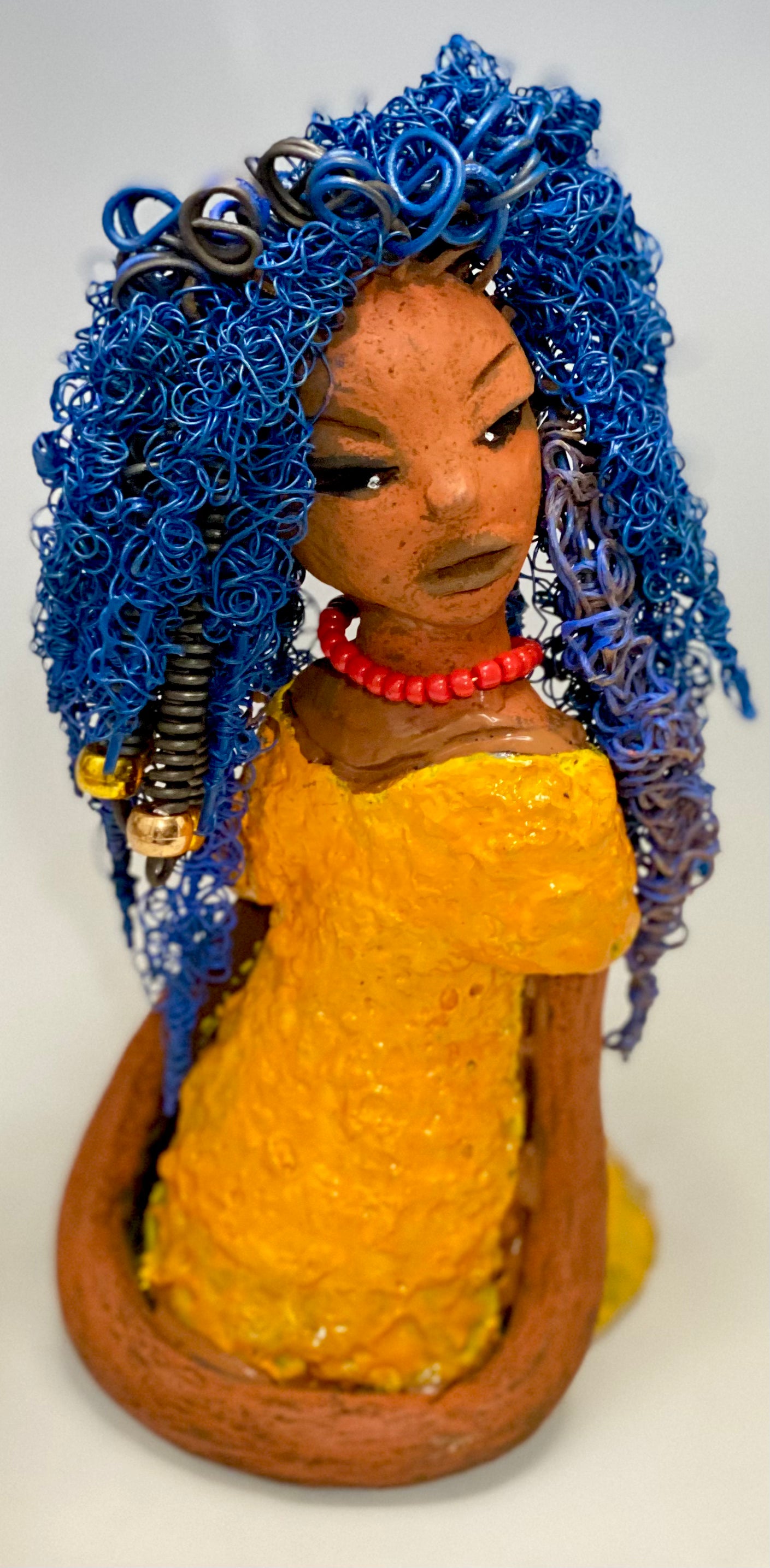 Makeba stands 8" x 5" x 5" and weighs 1.4 lbs. She has a lovely honey brown complexion with cocoa red lips. She has long twisted blue wire locs hairstyle waist down! Makeba has a sunset yellow red glazed dress. She has over 75 feet of 16 and 24 gauge blue wire for hair. It took over 5 hours just to do her hair! With eyes wide opened and a subdue look, Makeba has hope of finding a new home.