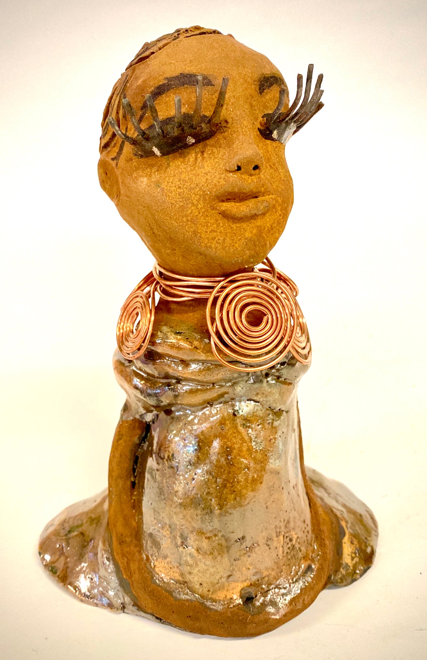 Charlotte stands 7" x 5" x 4" and weighs 1.03 lbs. She has a lovely honey brown complexion with reddish brown lips. She has a braided hairstyle. Charlotte has a colorful metallic yellow green antique copper glazed dress. She wears a spiral copper wire necklace. With eyes slightly opened, Charlotte has hopes of finding a new home.