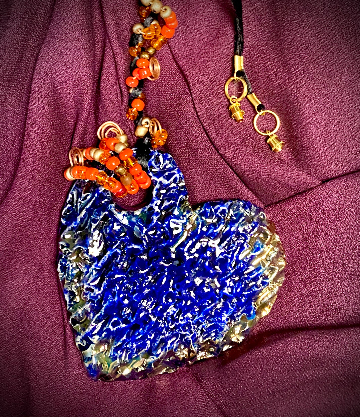 Have A Heart ! Each heart pendant is handmade with love! It is 3"x 3" and weighs approx. 3ozs. This pendant has a blue and gold metallic raku glazes that renders a unique translucent patina. The heart has a textured pattern . It holds a spiral of orange and red mini beads on a spiral copper wire. This pendant has a nice 12" black suede cord!