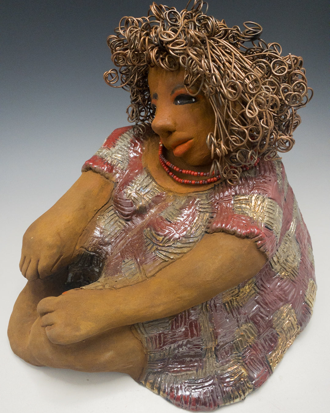 Introducing Rose! You'll be captivated by her irresistible charm! She's a curvy gal with a "herdew" hairstyle that I added some color to. Her honey rust complexion is absolutely lovely and she enhances it with rose-colored eye shadow. Her dress features bold red and gold geometric patterns and is textured for a unique touch. Rose's long arms are gently folded on her lap. Her hair is made of curly 16 gauge black wire and was carefully styled for a playful look. Measuring approximately 11" x 13" x 13" and wei