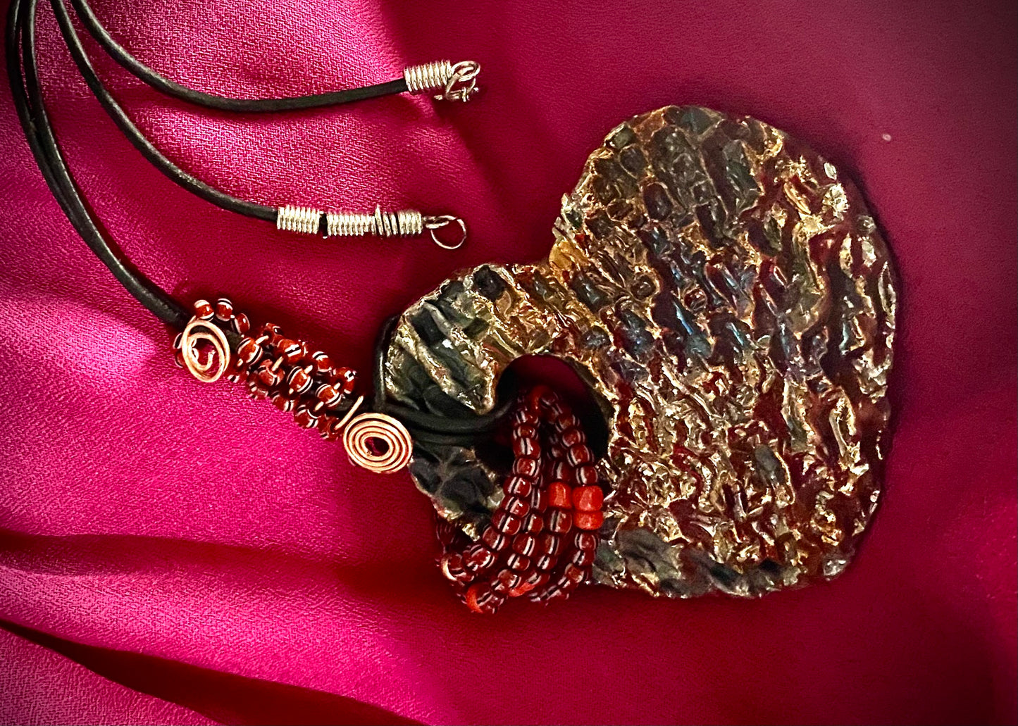 Have A Heart ! Each heart pendant is handmade with love! It is 3"x 3" and weighs approx. 3ozs. This pendant has a gold metallic raku glazes that renders a unique translucent patina. The heart has a textured pattern. It holds a spiral of ruby mini beads on a spiral copper wire. This pendant has a nice 12" black suede cord!