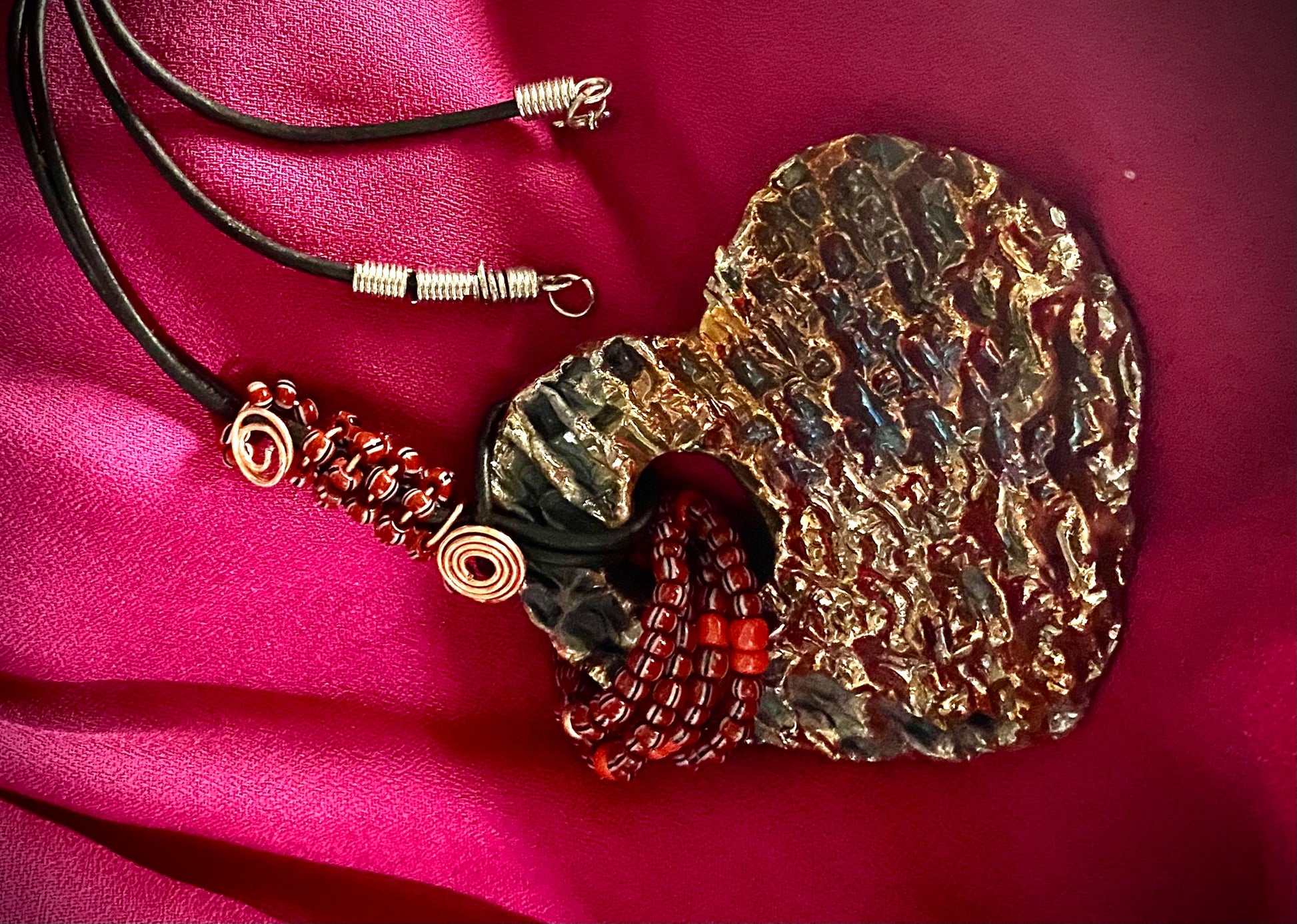 Have A Heart ! Each heart pendant is handmade with love! It is 3"x 3" and weighs approx. 3ozs. This pendant has a gold metallic raku glazes that renders a unique translucent  patina. The heart has a textured  pattern. It holds a spiral of ruby mini beads on a spiral copper wire. This pendant has a nice 12" black suede cord!