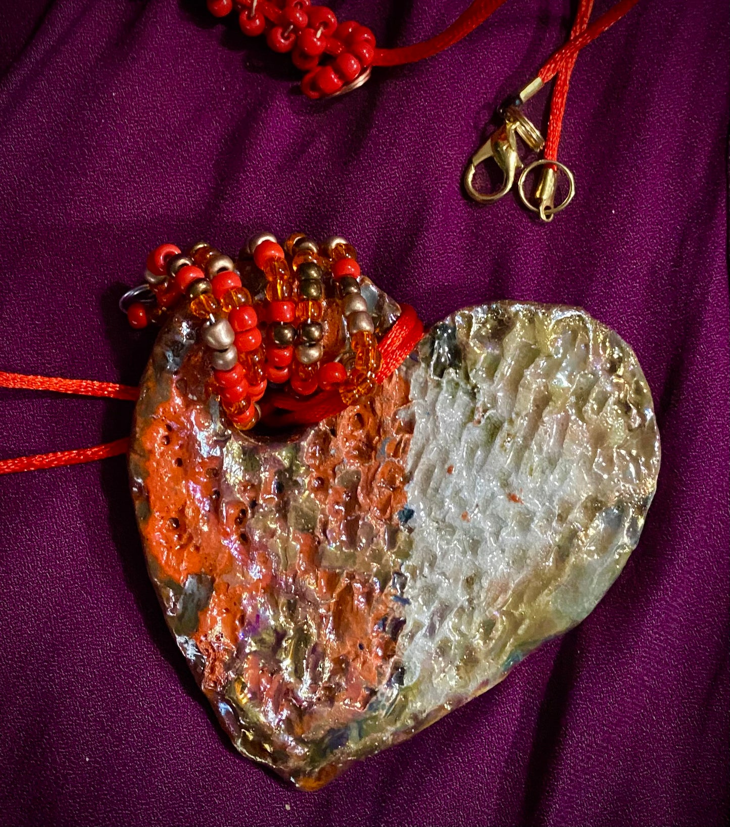 Have A Heart! Each heart pendant is handmade with love! It is 3"x 3"and weighs approx. 3ozs. This pendant has a red,orange, white and copper metallic raku glazes that renders a unique translucent patina. The heart has a textured pattern . Both sides are are different and equally beautiful! There is a spiral of red mini beads on copper in the center. This pendant has a nice 12" red adjustable rattail cord!