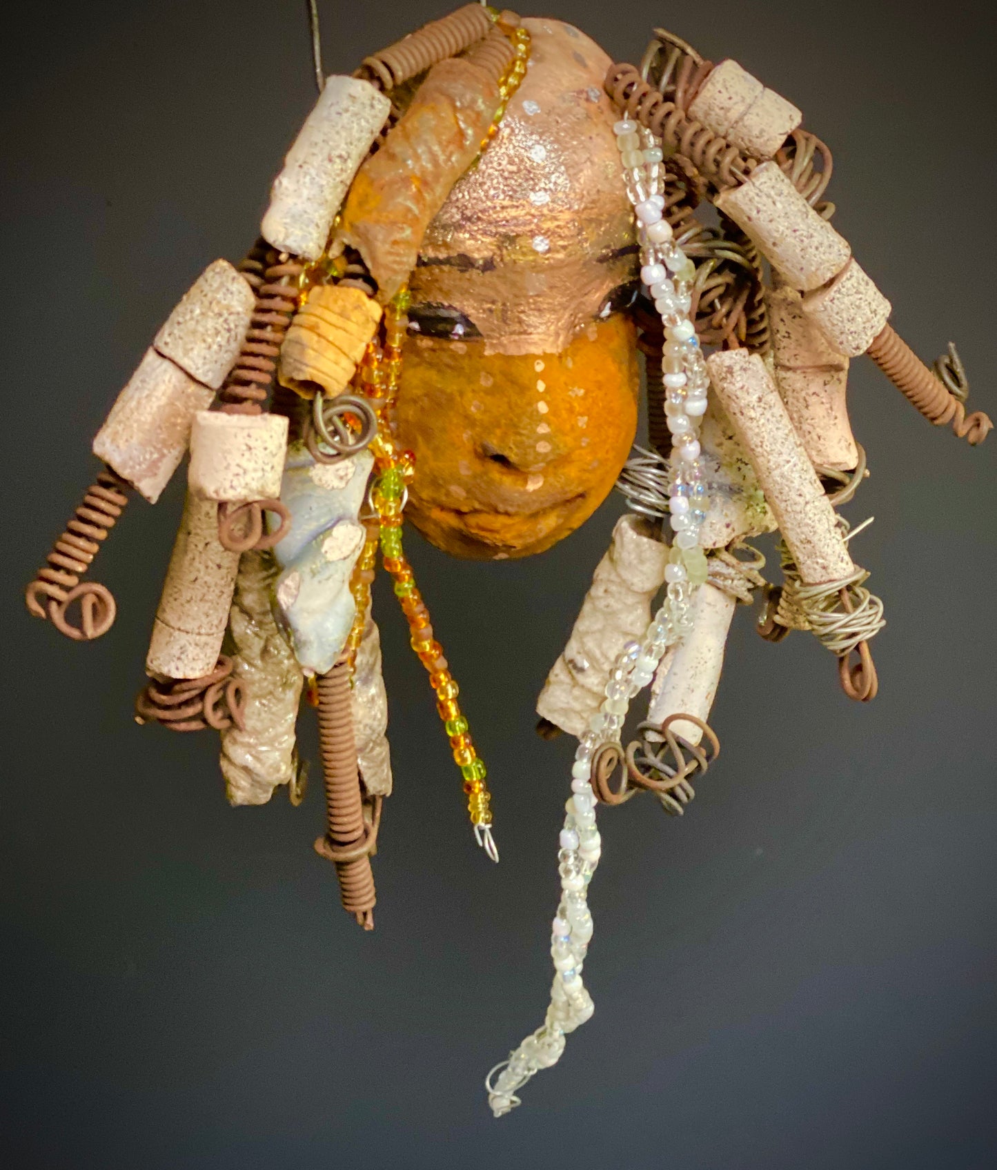I started making art soon after seeing authentic African artwork at the Smithsonian Museum of African Art. I was in total awe. Ryanna was inspired by my visit there. Ryanna is 8”x 6” and weighs 13 ozs. She has a two tone earthy honey and metallic gold complexion. Ryanna has over 20 raku beads and over a 100 mini colored and white beads spiral coils of hair. She more than 10 feet of 16 gauge wire hair