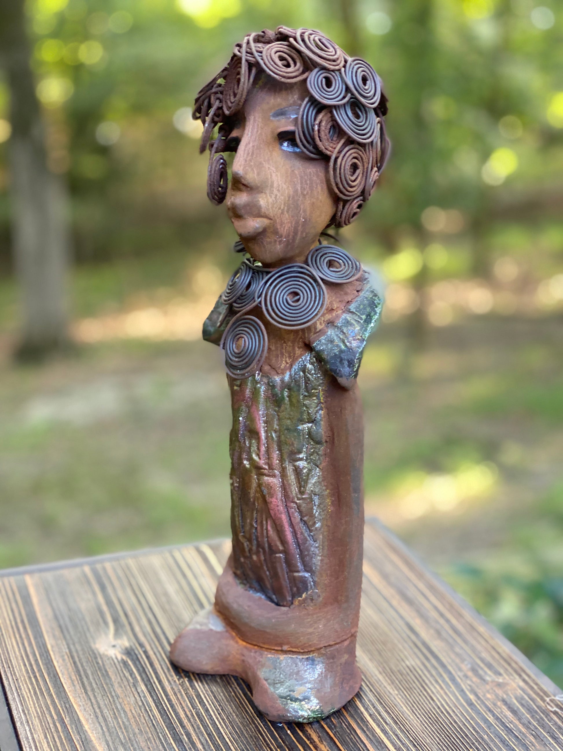 Meet Farida! Farida stand 13”x 5” x 4” and weighs 4 lbs. She has a bright eyes and a beautiful honey brown complexion. Farida has a fancy over the top Herdew. It took two hours to complete! A spiral 16 gauge necklace wraps around her neck. Her dress is a textured metallic green. Farida is looking for a new home.She would make a great gift to a BFF or just for YOU!