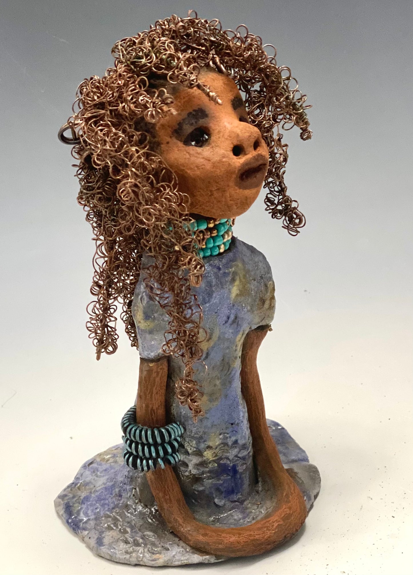 Meet Janae'! She has grown a head full of Hair! Janae' stands 8" x 5" x 4" and weighs 1.03 lbs. She has a lovely honey brown complexion with lovely reddish brown lips. Janae' wears a clay braided hairstyle. Janae' has a colorful metallic blue and gold glazed dress. She wears a blue and antique copper beaded necklace. With eyes wide opened, Janae' has hopes of finding a new home.
