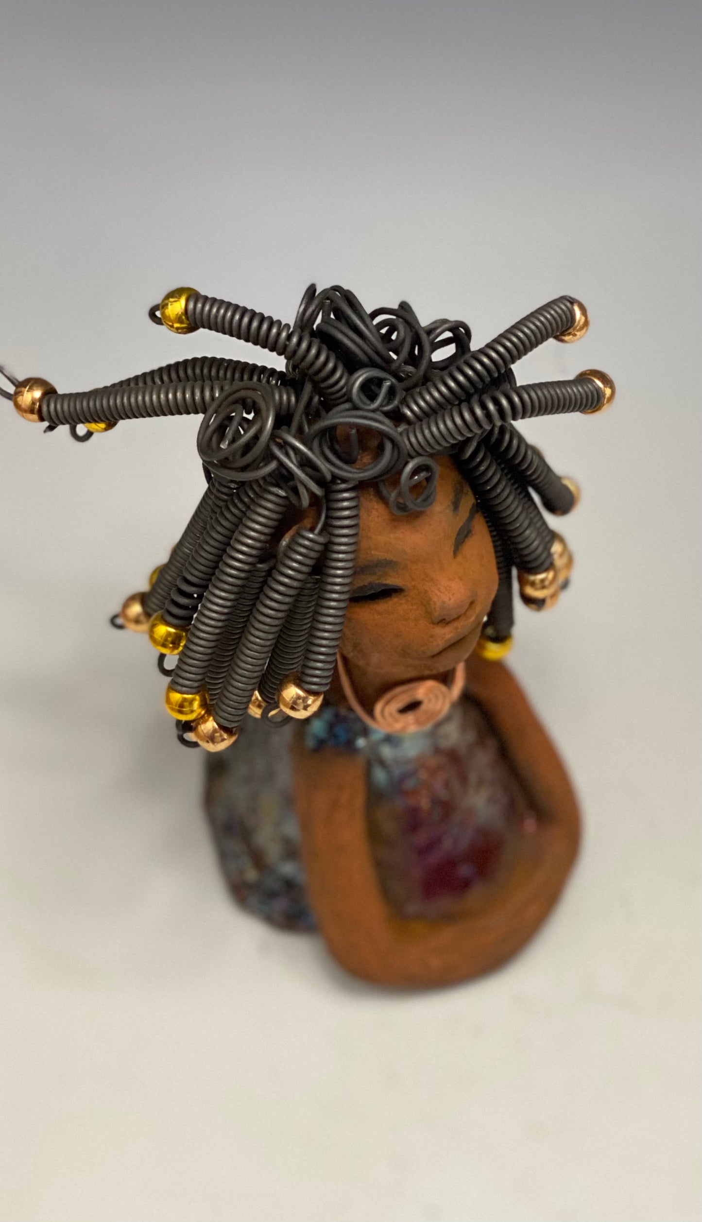 Meet Alexus Alexus stands 7.5" x 4" x 4" and weighs 1.05 lbs. She wears a lovely glossy metallic gold dress adorn by a spiral copper necklace. Alexus has over15 feet of coiled wire hair with gold beads.. Alexus appears to sit in a yoga pose. Her long arms rest at her side. Alexus is a great starter piece from the Herdew Collection!