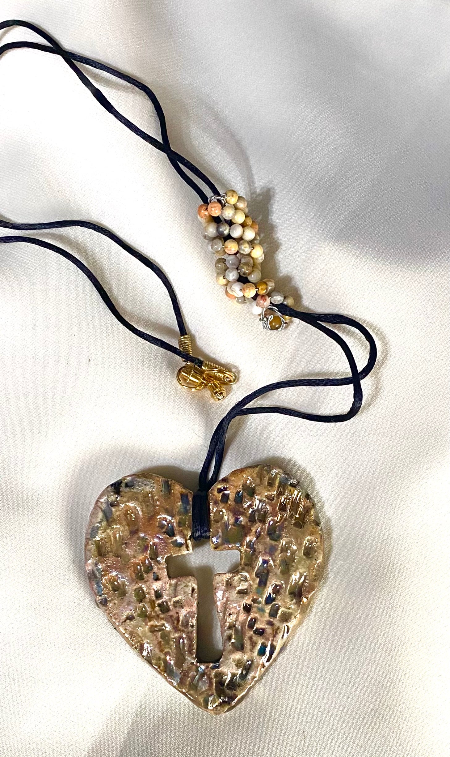 Have A Heart ! Each heart pendant is handmade with love! It is 3"x 3" and weighs approx. 3ozs. This pendant has a white and gold metallic raku glazes that renders a unique translucent  patina. The heart has a textured with cut out cross pattern . It holds a spiral of multicolored mini beads on a spiral copper wire. This pendant has a nice 12" black suede cord!
