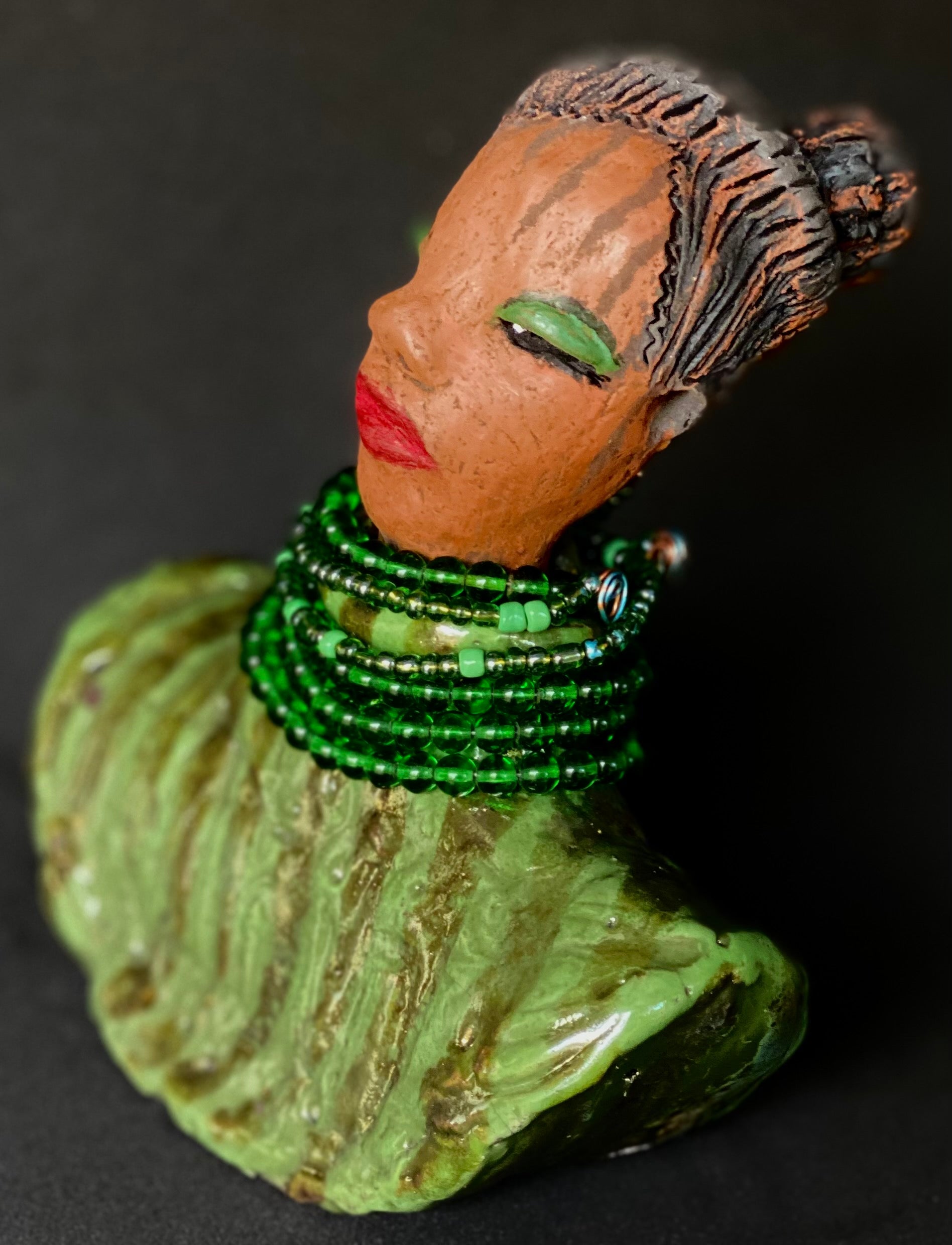 Delia looks up with joy and anticipation! Delia stands 7"x 6" x 3" and weighs 1.50 lbs. She wears an awesome metallic green textured copper robe. Delia has braided clay hair up in a bun. She has a honey brown complexion. Delia could make an excellent gift for your BFF! Delia will make for great conversation in your home. Free Shipping! Check out our Shipping  and Return policy