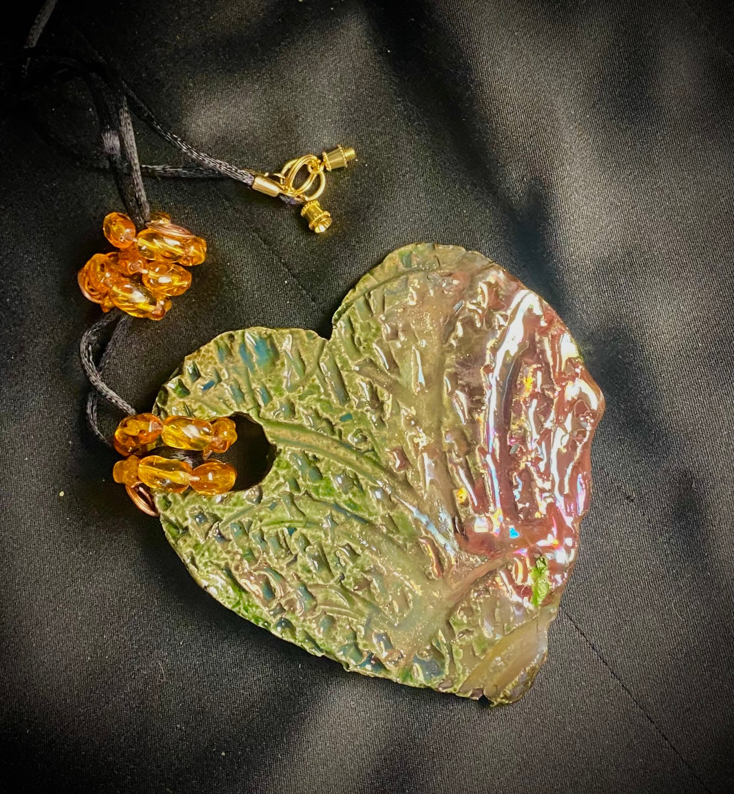 Have A Heart ! Each heart pendant is handmade with love! It is 3"x 3" and weighs approx. 3ozs. This pendant has an alligator green and gold metallic raku glazes that renders a unique translucent patina. The heart has a textured pattern. It holds a spiral of amber mini beads on a spiral copper wire. This pendant has a nice 12" black suede cord!