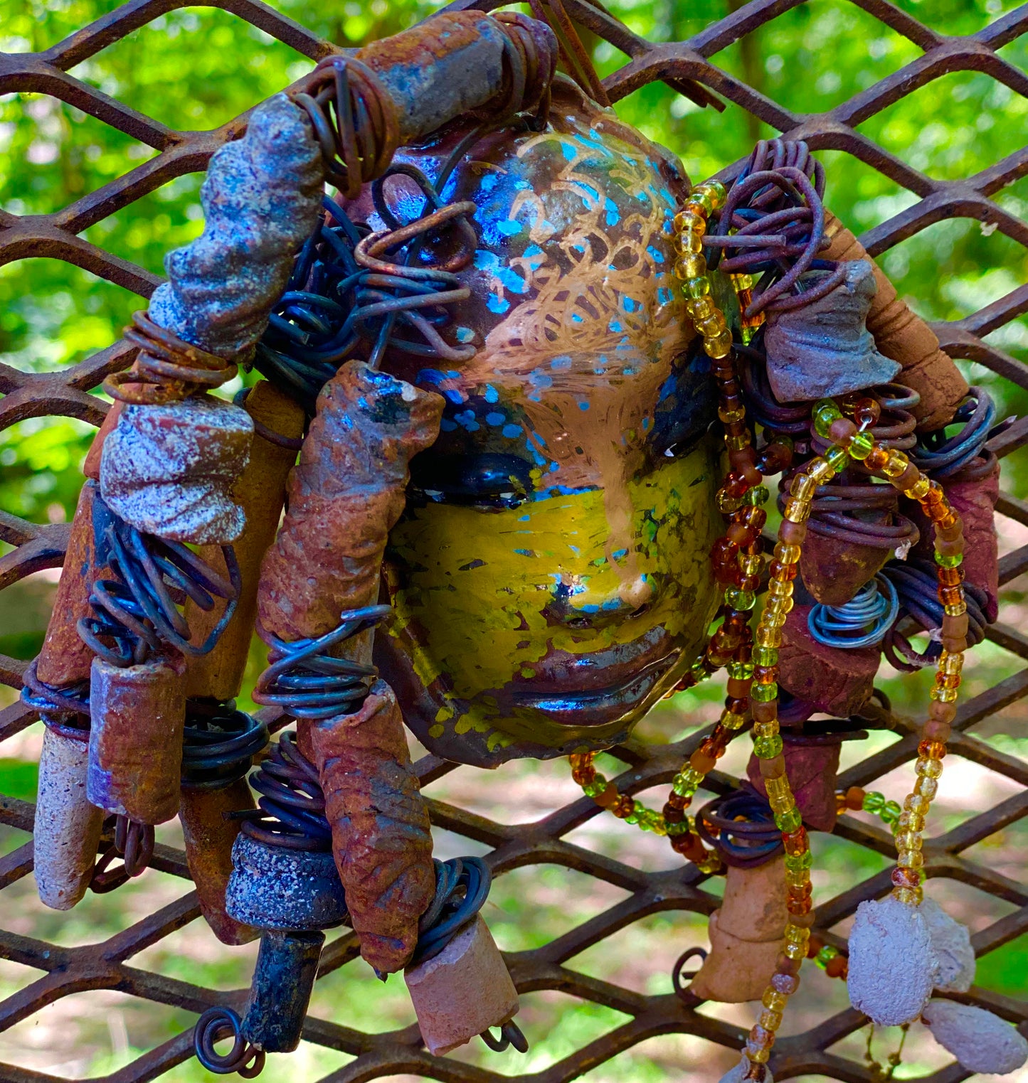 I started making mask soon after seeing authentic African artwork at the Smithsonian Museum of African Art. I was in total awe. Marali means she who listen was inspired by my visit there. Marali has a two tone metallic blue copper gold complexion. She is 7" x 5" and weighs 14 ozs. Marali has over 20 handmade raku fired beads. She has over 50 mini amber bead twisted as hair. Marali has over 6 feet of copper coiled 16 gauge wire hair.