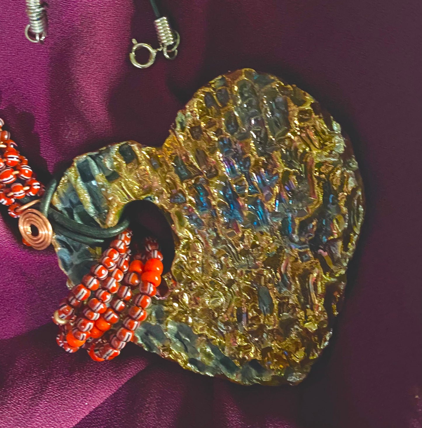 Have A Heart ! Each heart pendant is handmade with love! It is 3"x 3" and weighs approx. 3ozs. This pendant has a gold metallic raku glazes that renders a unique translucent patina. The heart has a textured pattern. It holds a spiral of ruby mini beads on a spiral copper wire. This pendant has a nice 12" black suede cord!