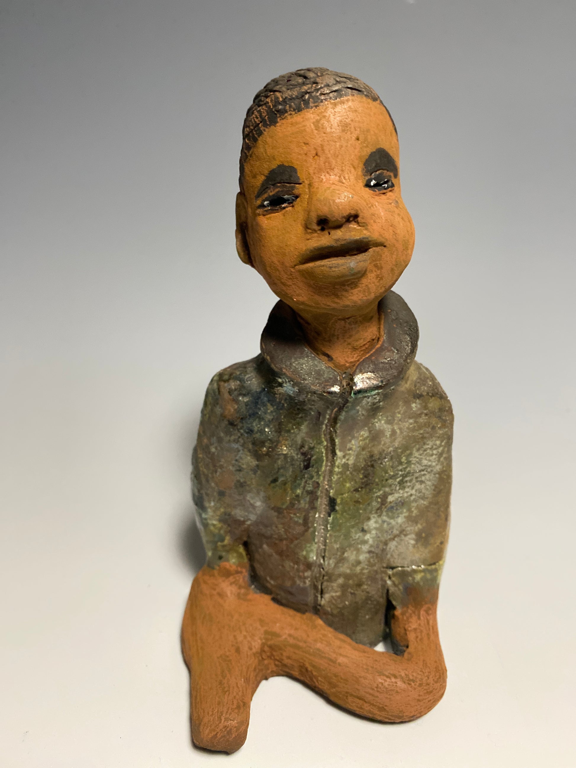 Ray is one happy studious teen who will lighten up a room!  Ray stands 7" x 3" x 3.5" and weighs 15 ozs. He has a metallic  green jacket with pull up collar . Ray complexion is honey brown. He has no facial hair and wears a bright smile. His arms are folded as he prepares to be invited into your home!