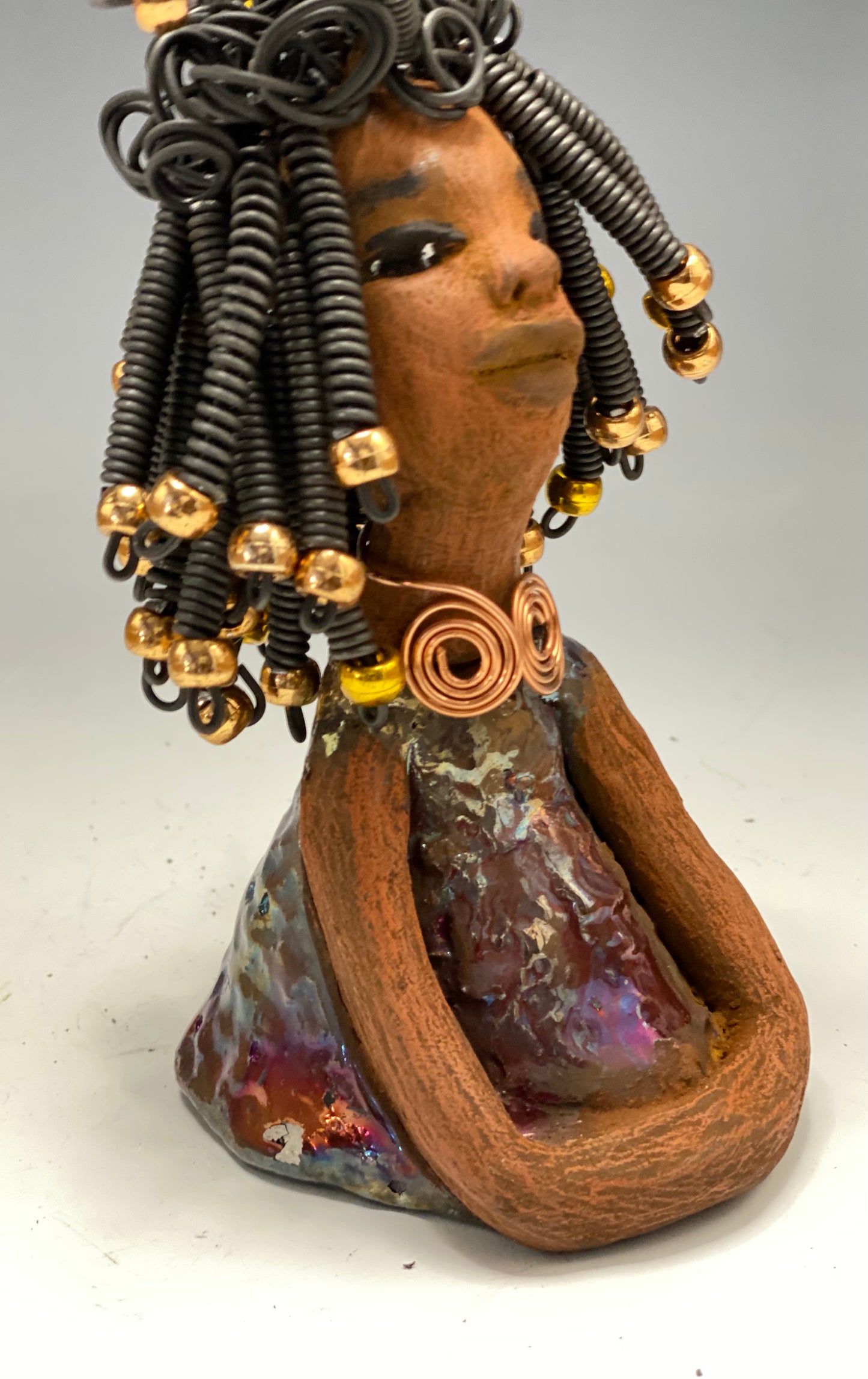 Meet Alexus Alexus stands 7.5" x 4" x 4" and weighs 1.05 lbs. She wears a lovely glossy metallic gold dress adorn by a spiral copper necklace. Alexus has over15 feet of coiled wire hair with gold beads.. Alexus appears to sit in a yoga pose. Her long arms rest at her side. Alexus is a great starter piece from the Herdew Collection!