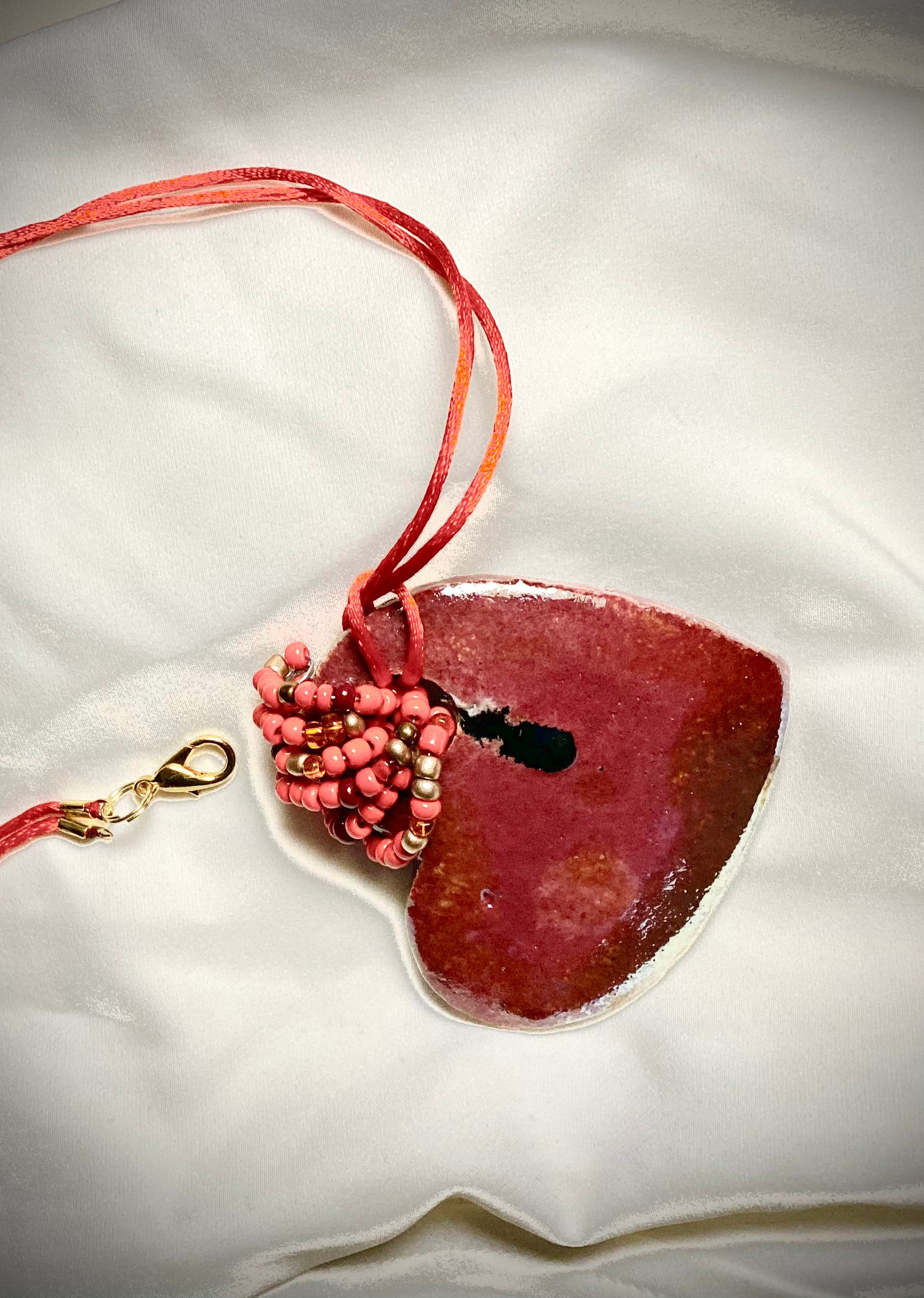 Each heart pendant is handmade with love! It is 3"x 3" and weighs approx. 3ozs. This pendant has a red violet and gold metallic raku glazes that renders a unique translucent  patina. The heart has a smooth surface . Both sides are  are different and equally beautiful! It holds a spiral of red violet mini beads on a spiral copper wire. This pendant has a nice 12" red suede cord!