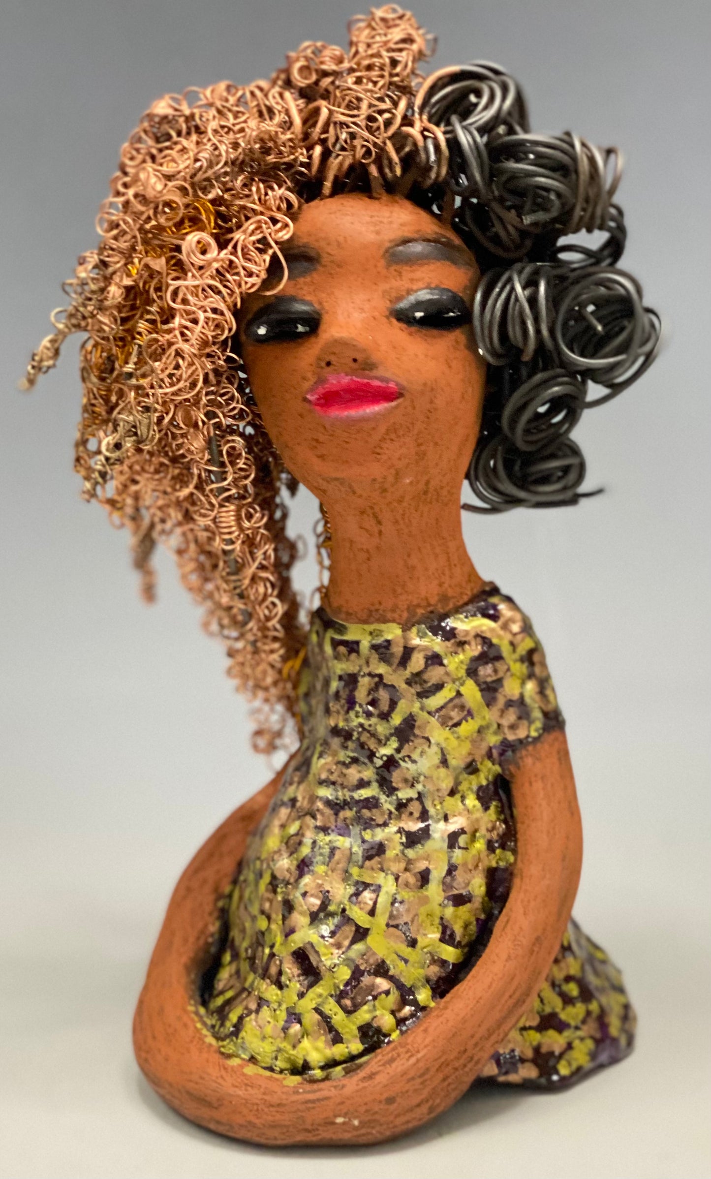 Meet Kalifa, an elegant figurine weighing 1.11 lbs and measuring 8" x 5" x 5.5". Her glossy spotted metallic copper glazed dress and long twisted wire locs are expertly crafted. With her honey brown complexion and red lips, she is sure to capture the attention of your guests. Her daring two-tone copper hair, which took 6 hours to create, adds to her beauty. Invite her into your home and spark meaningful conversations with her cheerful eyes and hopeful gaze.
