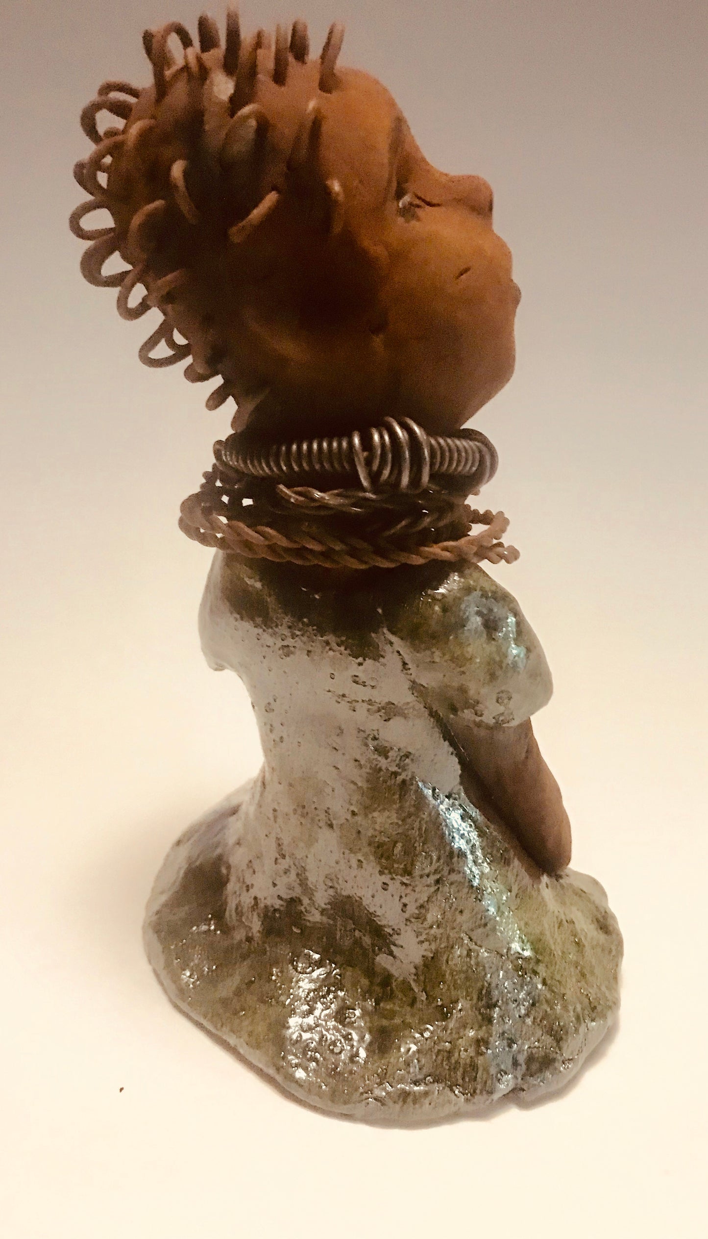 Nura stands 7.5" x 5" x 5" and weighs 1.06 lbs. She has a lovely honey brown complexion with reddish brown lips. She has a wire braided hairstyle. Nura has a colorful metallic green antique copper glazed dress. She wears spiral wire necklaces With her eyes wide opened, Nura has hopes of finding a new home.