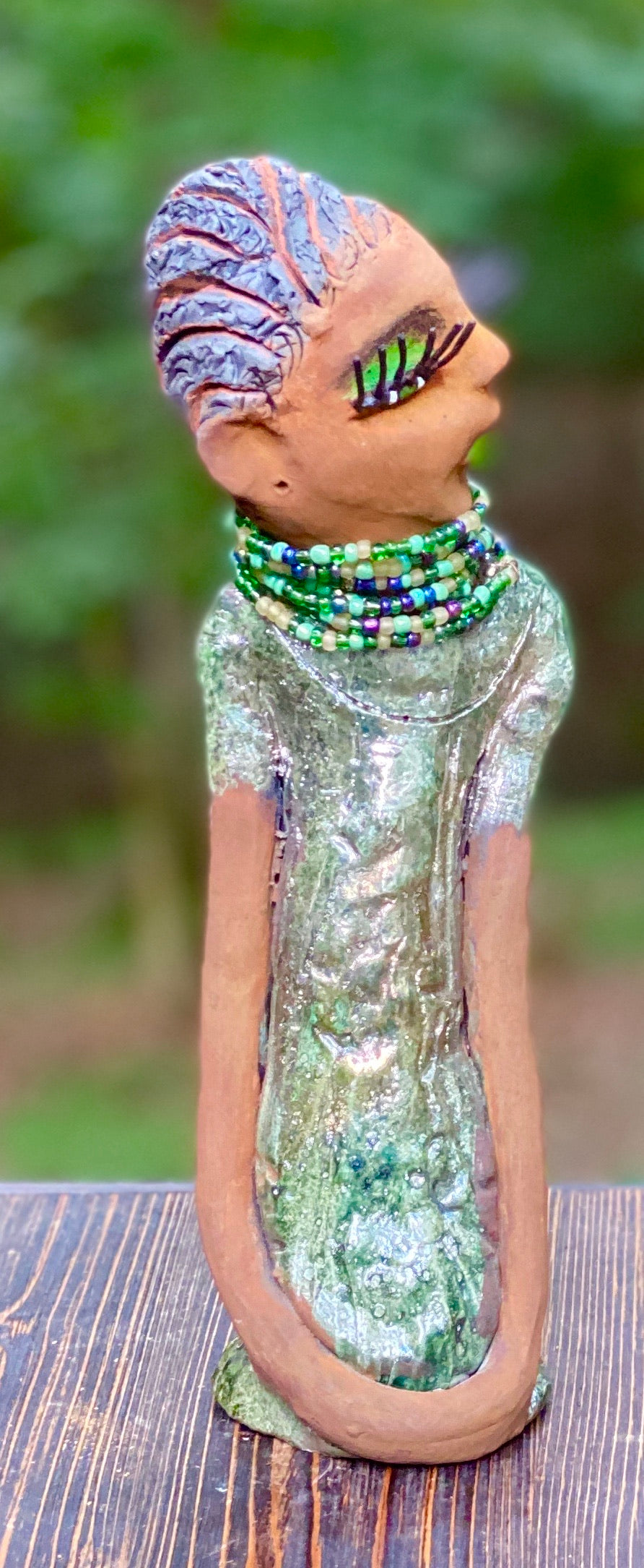 Meet Marissa! Marissa stands 11.5" x 3" x 3.5" and weighs 2.5 lbs. She has a lovely honey brown complexion with reddish brown lips. She has a braided short black clay hairstyle. Marissa has a colorful metallic copper green antique glazed dress. She wears the world's longest eyelashes. With her green eyes slightly opened, Marissa has hope of finding her way into your home.