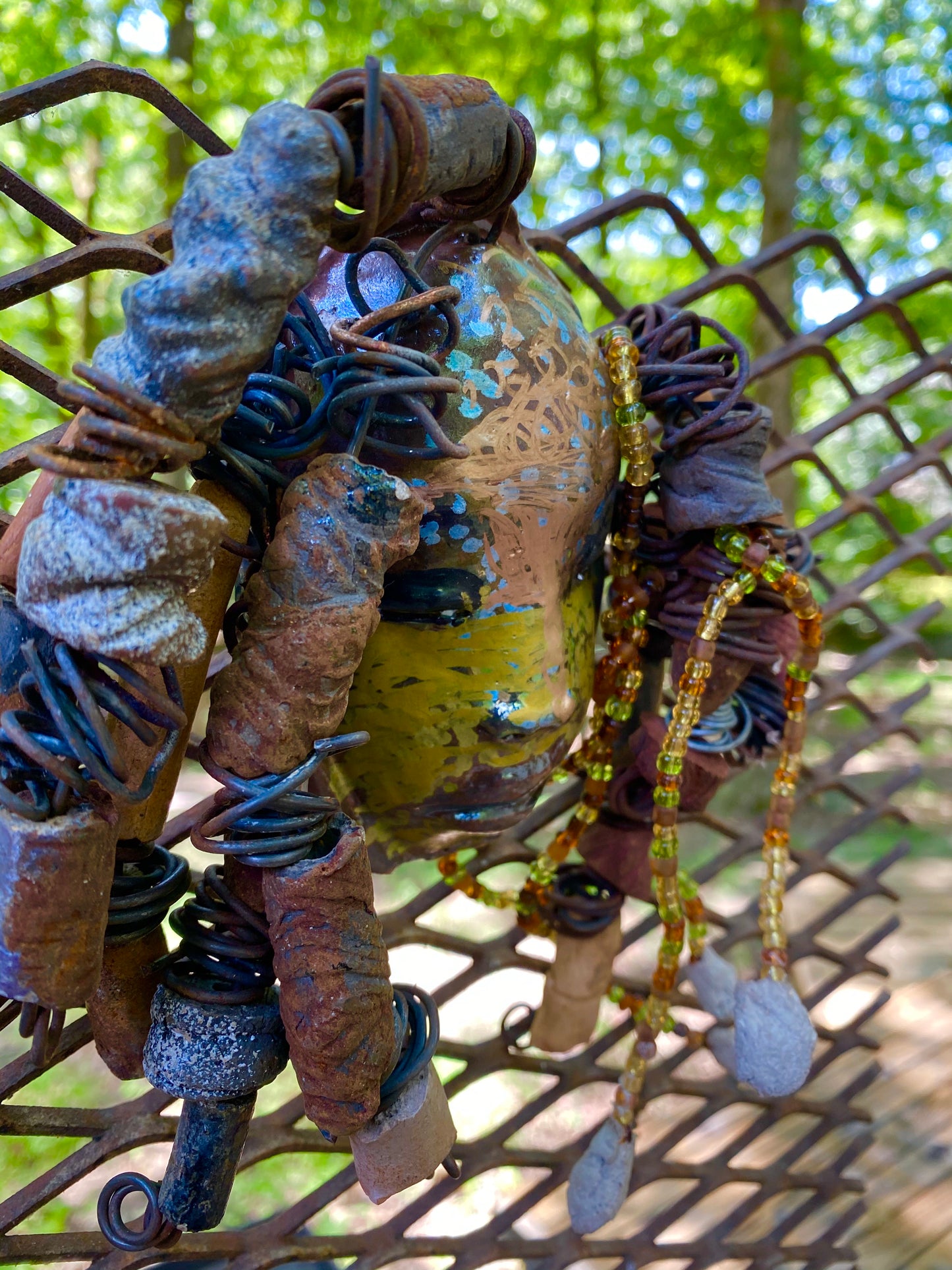 I started making mask soon after seeing authentic African artwork at the Smithsonian Museum of African Art. I was in total awe. Marali means she who listen was inspired by my visit there. Marali has a two tone metallic blue copper gold complexion. She is 7" x 5" and weighs 14 ozs. Marali has over 20 handmade raku fired beads. She has over 50 mini amber bead twisted as hair. Marali has over 6 feet of copper coiled 16 gauge wire hair.