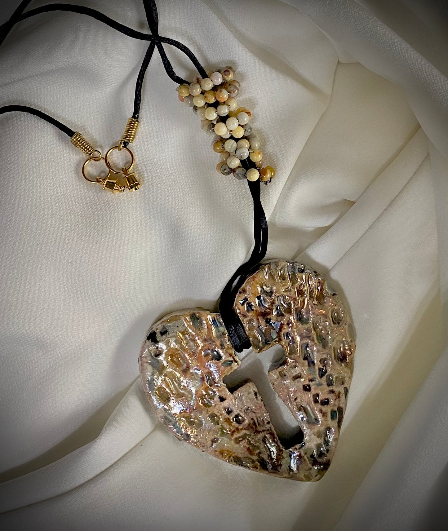 Have A Heart ! Each heart pendant is handmade with love! It is 3"x 3" and weighs approx. 3ozs. This pendant has a white and gold metallic raku glazes that renders a unique translucent patina. The heart has a textured with cut out cross pattern . It holds a spiral of multicolored mini beads on a spiral copper wire. This pendant has a nice 12" black suede cord!