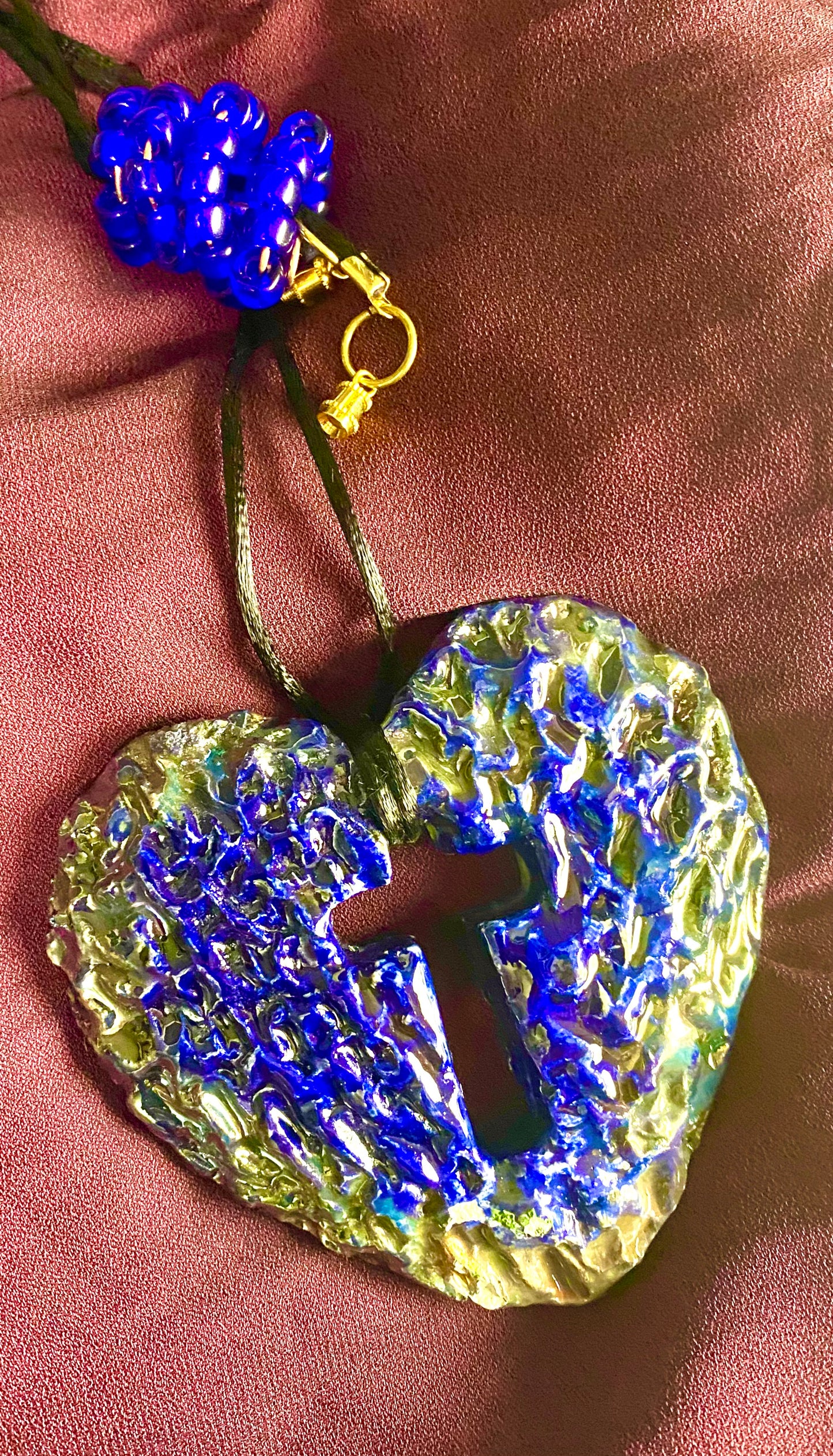 Have A Heart ! Each heart pendant is handmade with love! It is 3"x 3" and weighs approx. 3ozs. This pendant has a royal blue and gold metallic raku glazes that renders a unique translucent patina. The heart has a cut out cross in the center with a textured pattern. It holds a spiral of royal blue mini beads on a spiral copper wire. This pendant has a nice 12" black suede cord!