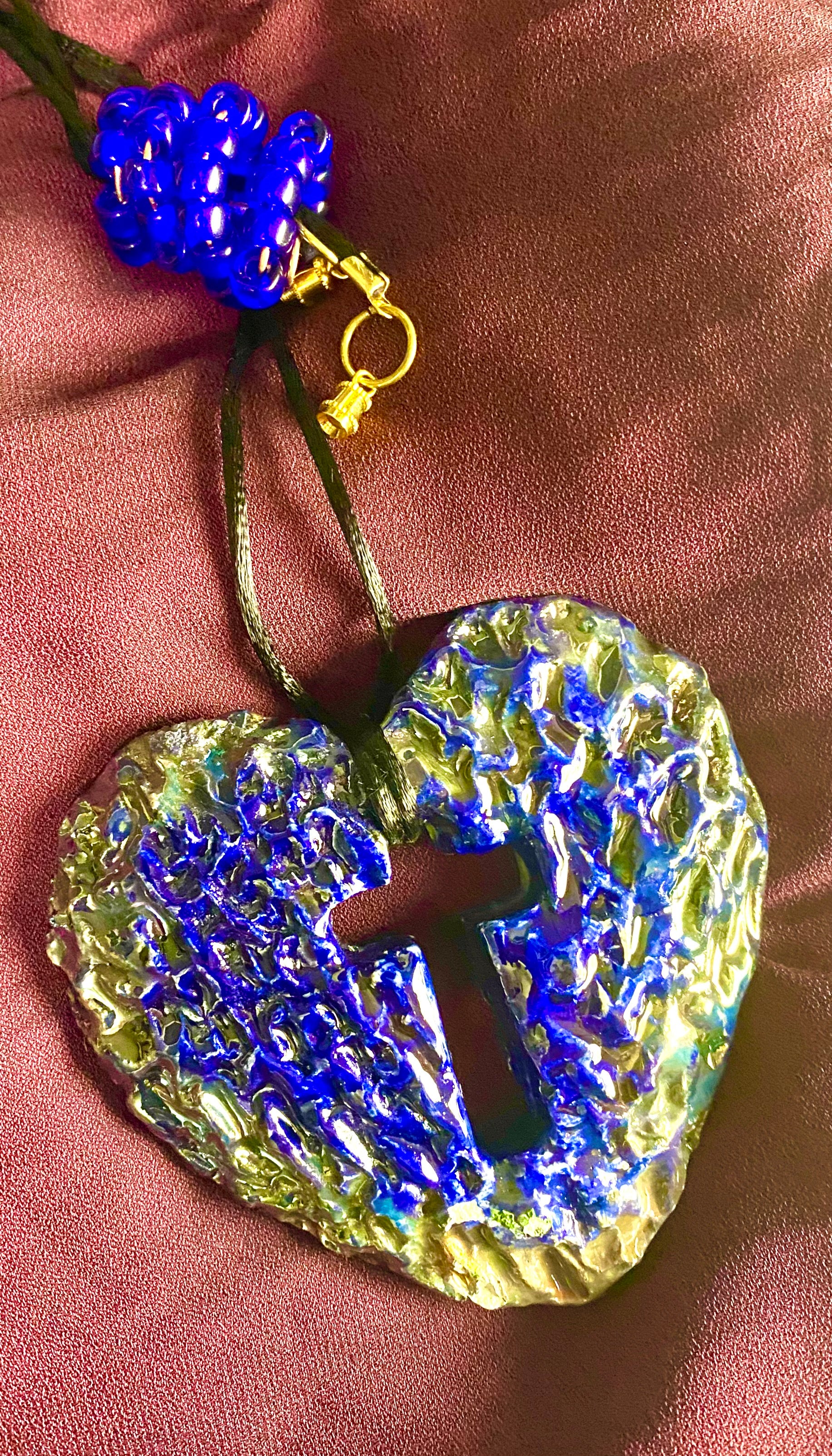 Have A Heart ! Each heart pendant is handmade with love! It is 3"x 3" and weighs approx. 3ozs. This pendant has a royal blue and gold metallic raku glazes that renders a unique translucent  patina. The heart has a cut out cross in the center with a textured  pattern. It holds a spiral of royal blue mini beads on a spiral copper wire. This pendant has a nice 12" black suede cord!