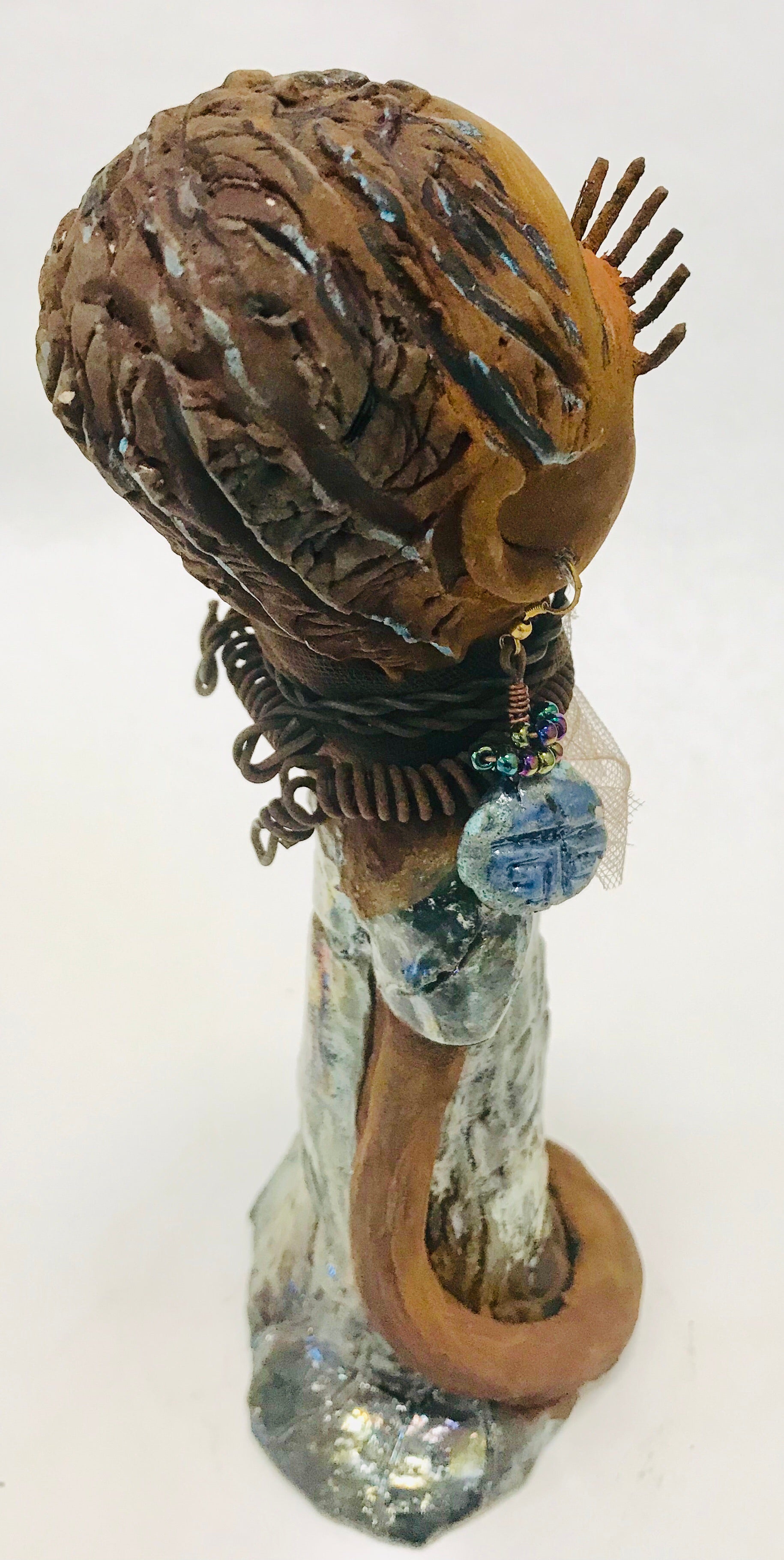 Sorbari stands 11" x 4" x 4" and weighs 2.5 lbs. She has a lovely honey brown complexion with  reddish brown lips. She has a braided hairstyle.  Sorbari has a colorful metallic green antique copper glazed dress. She wears two spiral wire necklaces. With long eyes slightly opened, Sorbari has hopes of finding a new home.