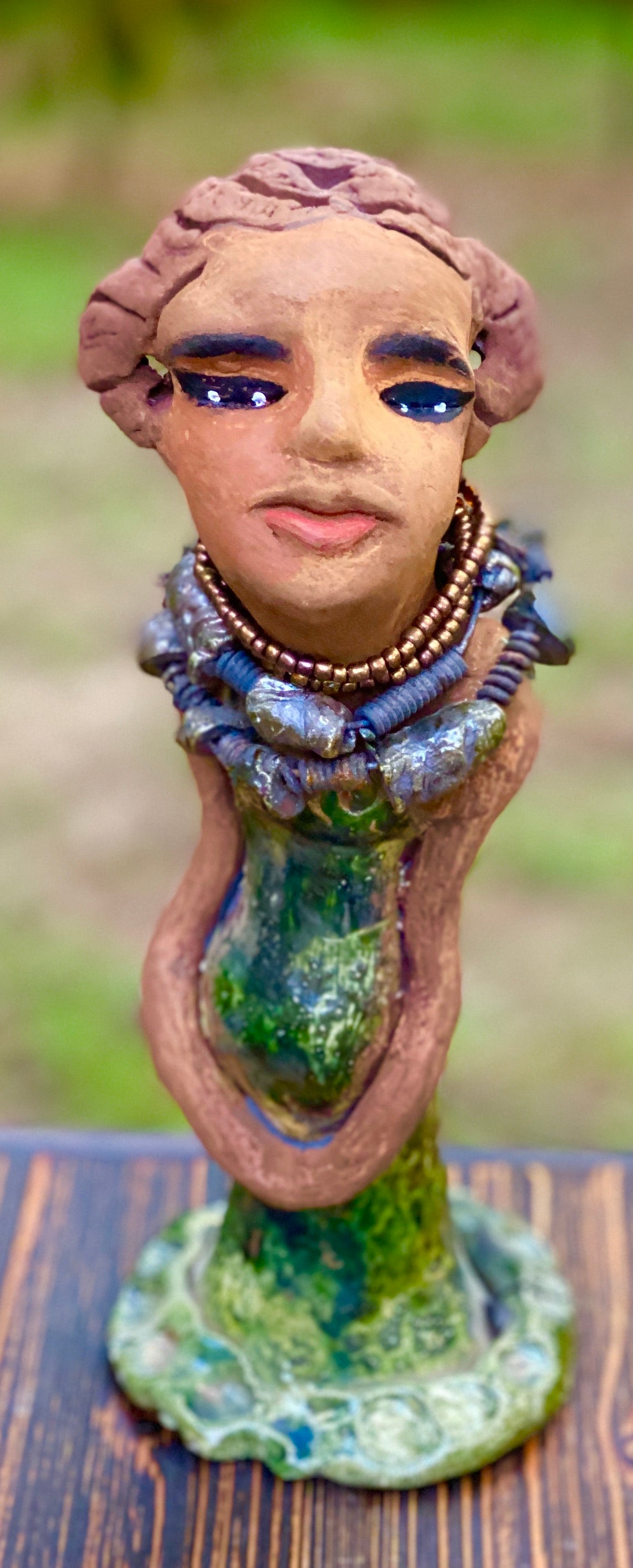 Greta! Greta stands 11" x 4" x 4" and weighs 2.5 lbs. She has a lovely honey brown complexion with reddish brown lips. She has a braided hairstyle. Gretaya has a colorful metallic green antique copper glazed dress. She wears two raku beaded necklaces. With long eyes slightly opened, Greta has hopes of finding a new home.