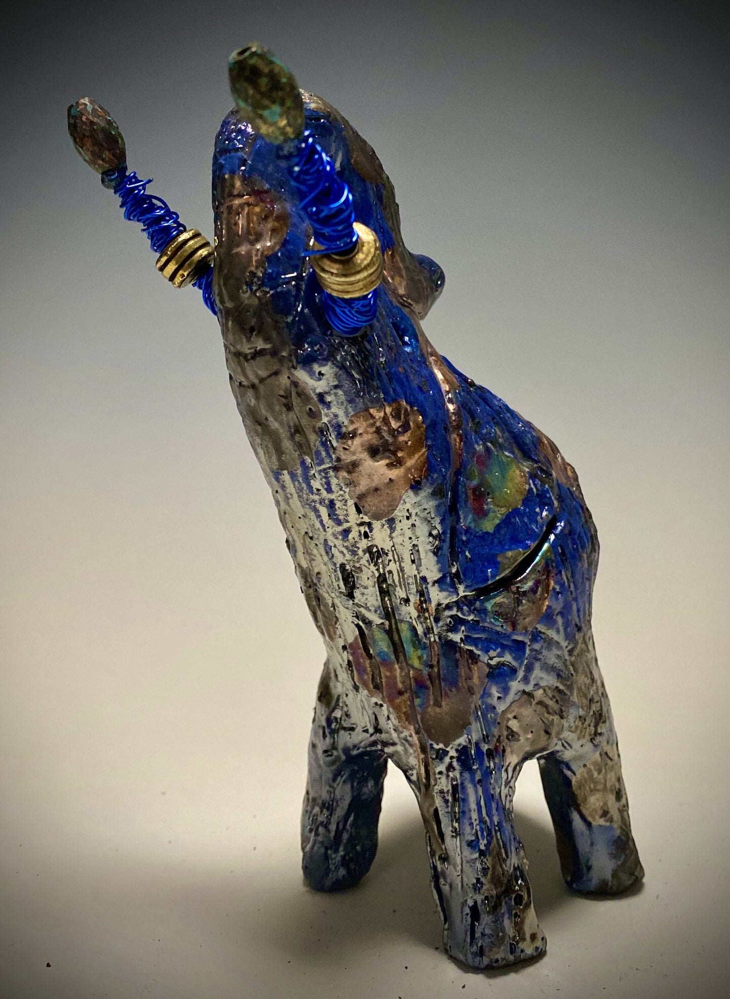 Raku Elephant Have you HERD!!!!!! Just one of these lovely Raku Fired Elephant will make an excellent gift for your friend, sorority or for your home’ special place centerpiece. 7" x 4" x 4" 14 ozs. Blue wire beaded blue tusk Beautiful metallic raku colors For decorative purposely only.