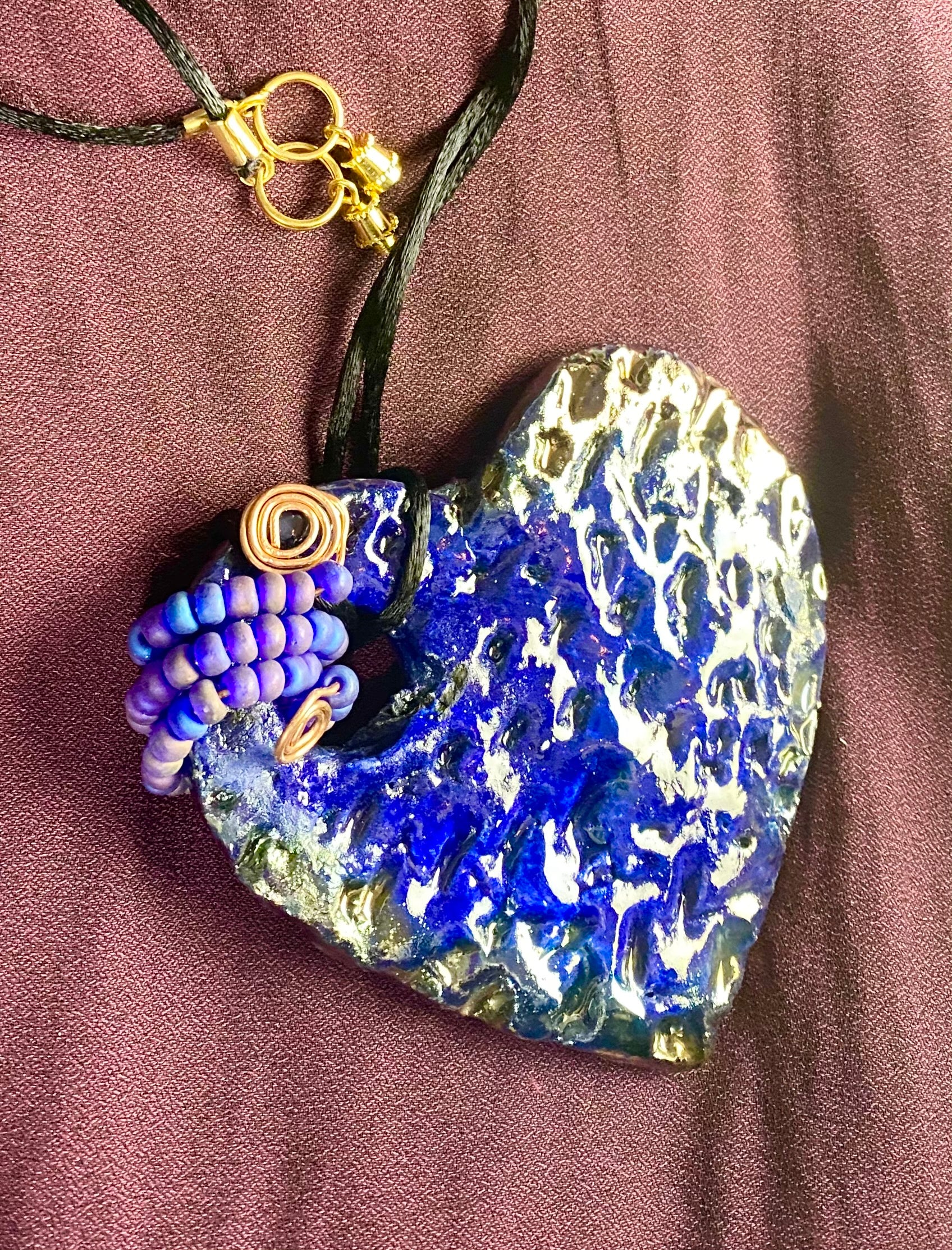 Have A Heart ! Each heart pendant is handmade with love! It is 3"x 3" and weighs approx. 3ozs. This pendant has a royal blue and gold metallic raku glazes that renders a unique translucent  patina. The heart  has a textured  pattern. It holds a spiral of off blue violet mini beads on a spiral copper wire. This pendant has a nice 12" black suede cord!