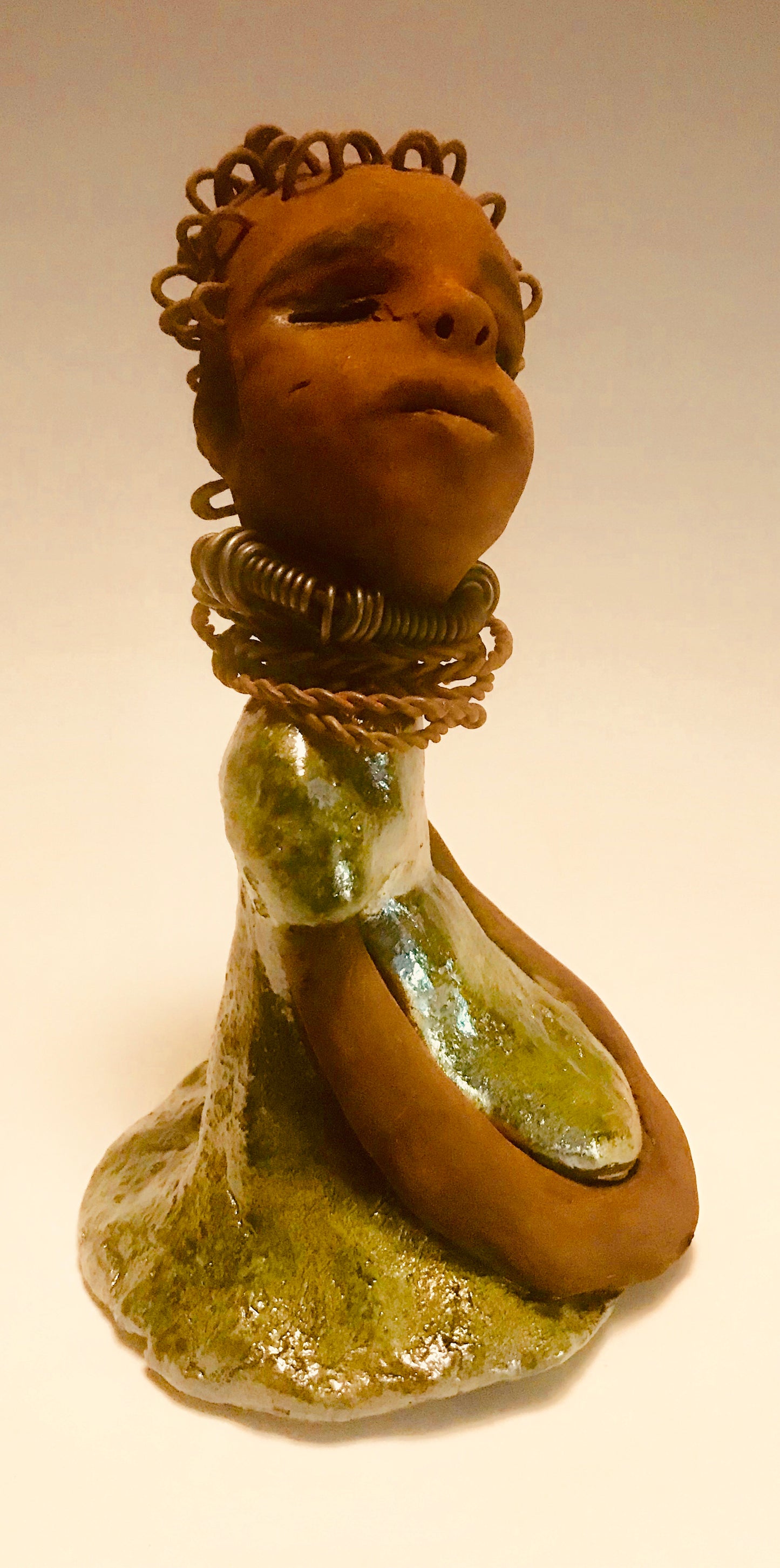 Nura stands 7.5" x 5" x 5" and weighs 1.06 lbs. She has a lovely honey brown complexion with reddish brown lips. She has a wire braided hairstyle. Nura has a colorful metallic green antique copper glazed dress. She wears spiral wire necklaces With her eyes wide opened, Nura has hopes of finding a new home.