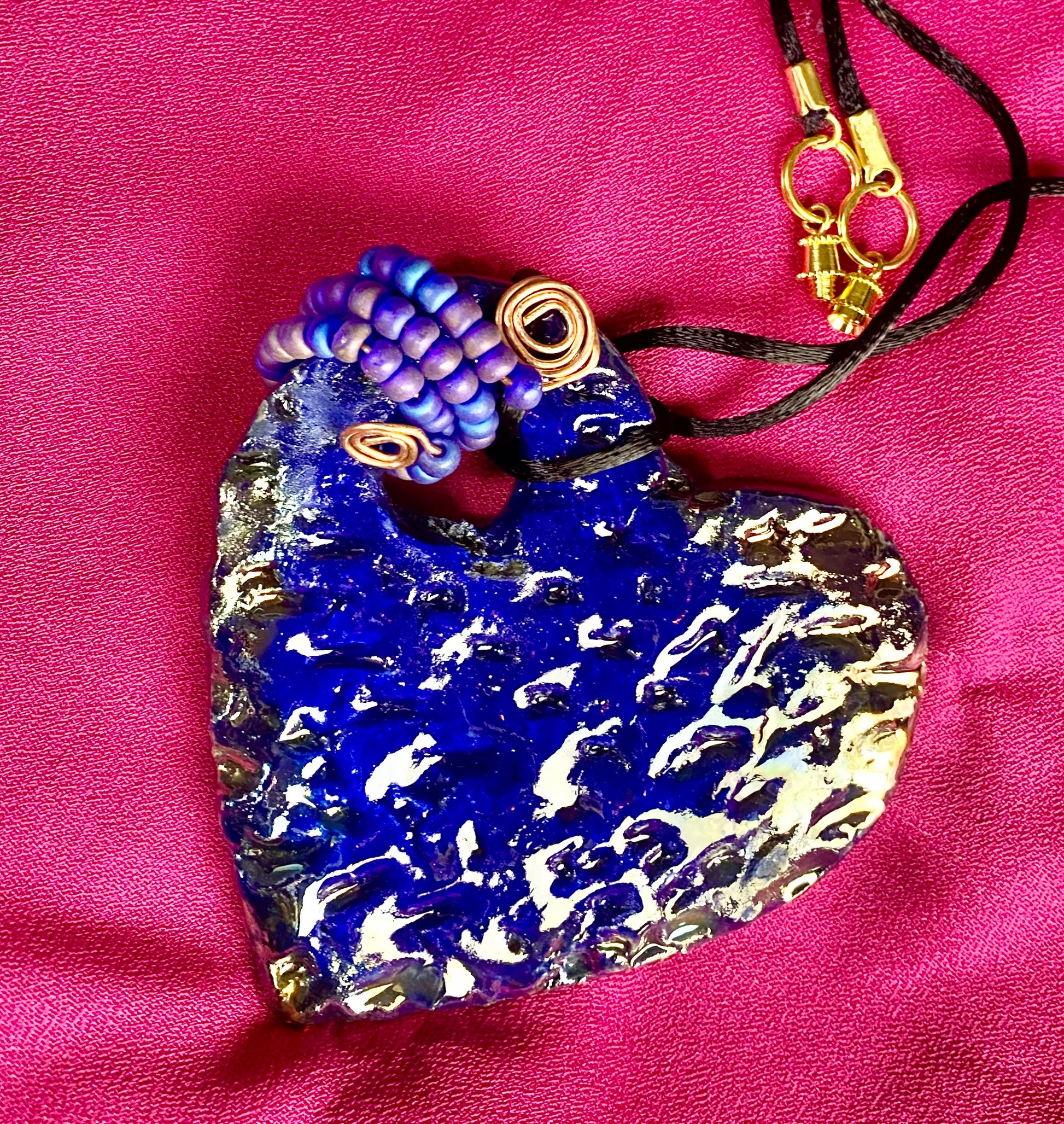 Have A Heart ! Each heart pendant is handmade with love! It is 3"x 3" and weighs approx. 3ozs. This pendant has a royal blue and gold metallic raku glazes that renders a unique translucent  patina. The heart  has a textured  pattern. It holds a spiral of off blue violet mini beads on a spiral copper wire. This pendant has a nice 12" black suede cord!