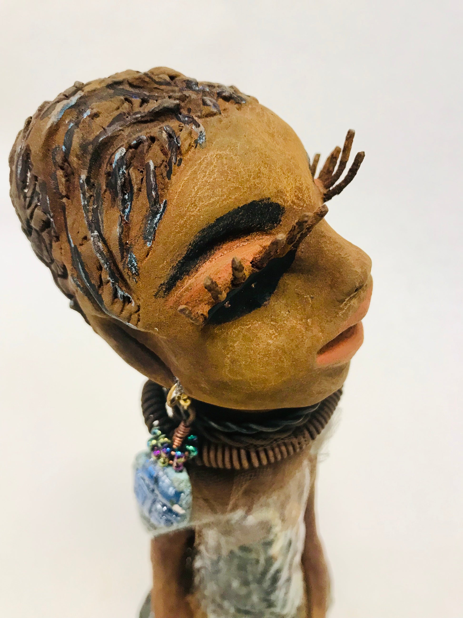 Sorbari stands 11" x 4" x 4" and weighs 2.5 lbs. She has a lovely honey brown complexion with  reddish brown lips. She has a braided hairstyle.  Sorbari has a colorful metallic green antique copper glazed dress. She wears two spiral wire necklaces. With long eyes slightly opened, Sorbari has hopes of finding a new home.
