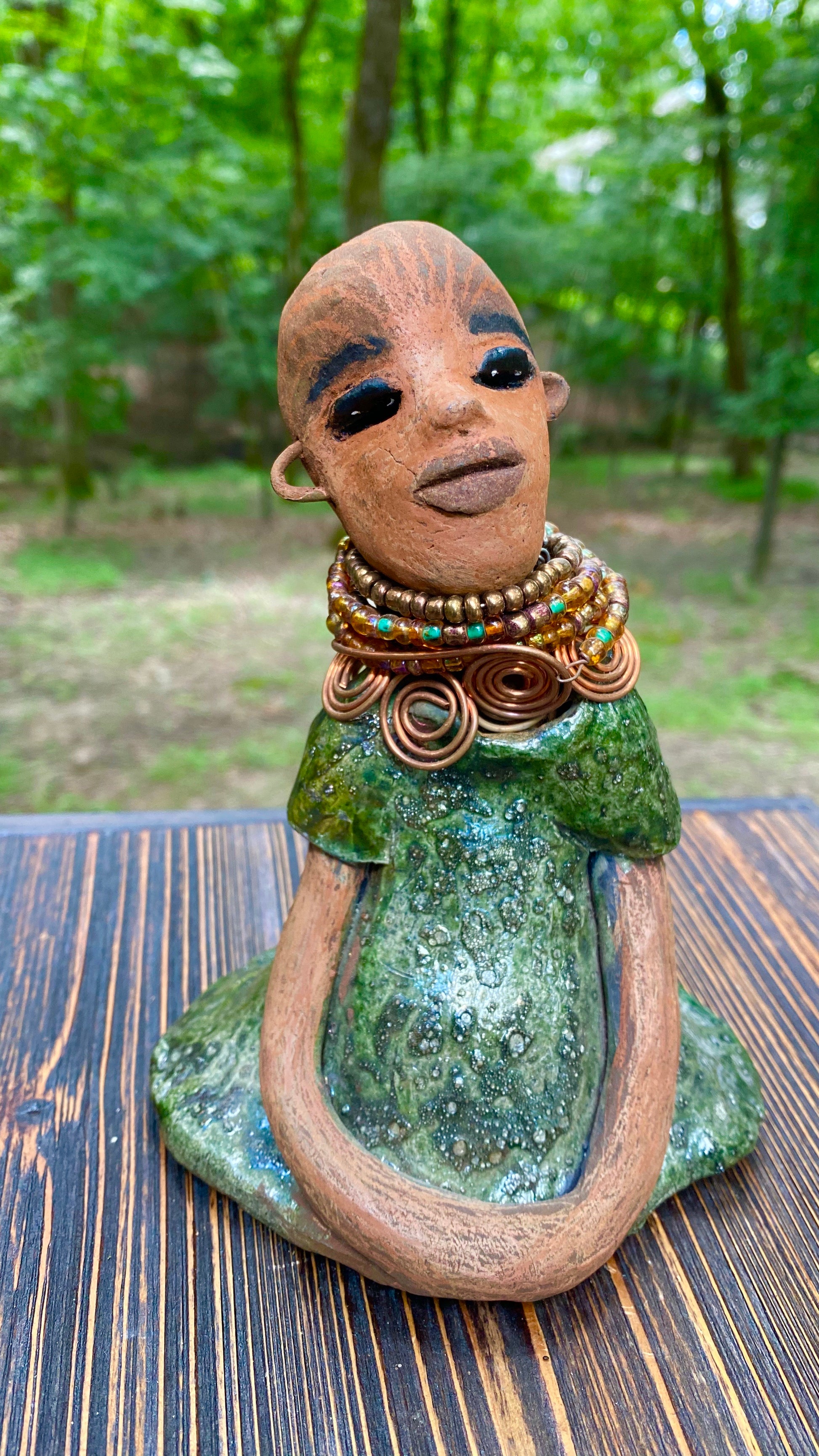Meet Faye! Faye stands 7" x 5" x 4" and weighs 2.3 lbs. She has a lovely two tone honey brown complexion with  chocolate brown lips. She has a braided hairstyle.  Faye has a colorful metallic green antique glazed dress. She wears an awesome beaded collar with a copper spiral necklace. Her long loving arms rest at her side. With eyes wide opened, Faye has hopes of finding a new home.