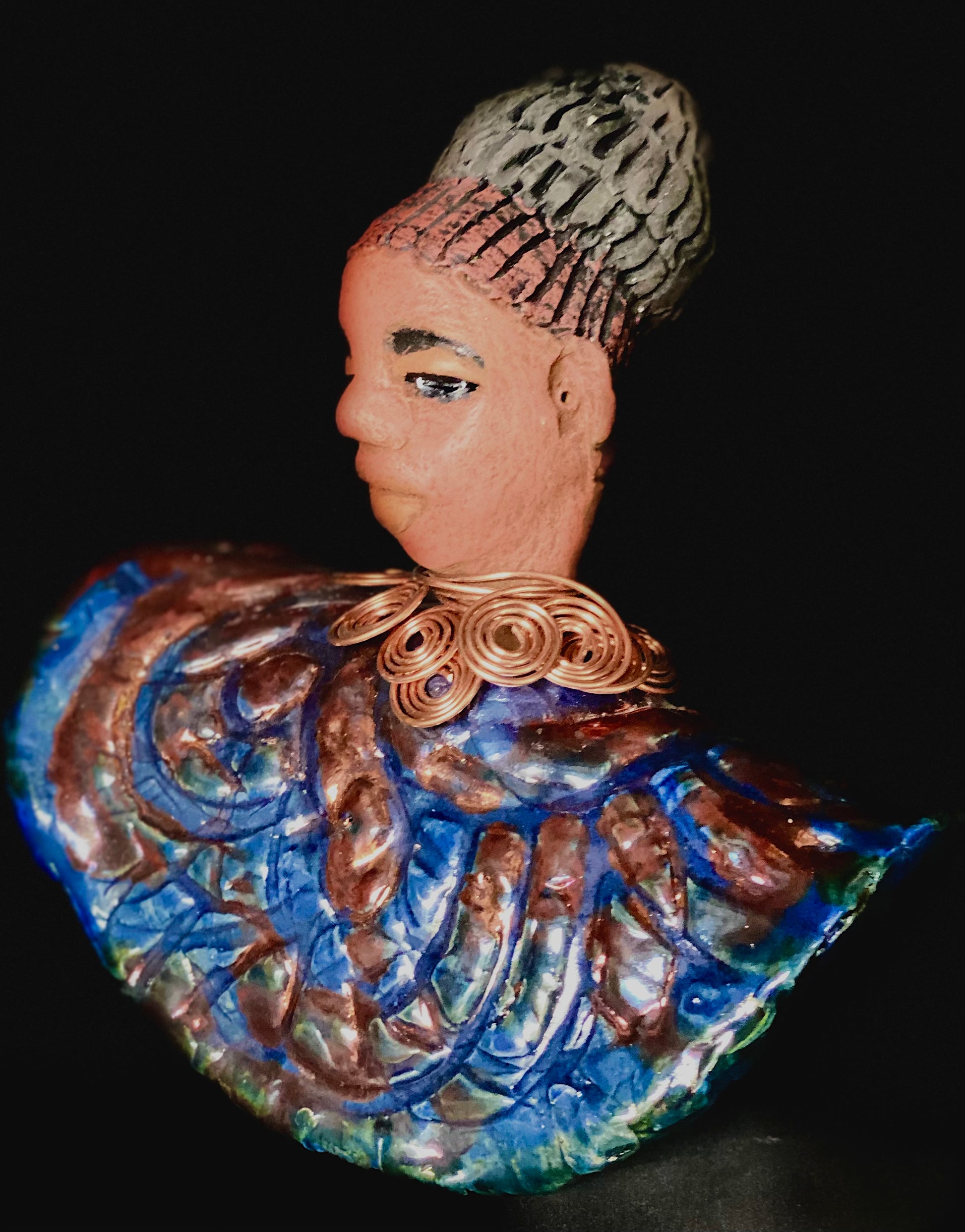 Meet Tia! Tia looks up with joy and anticipation! Tia stands 7" x 6" x 4" and weighs 1.90 lbs. She has a beautiful textured copper and blue robe. Tia has braided clay hair up in a bun. She has a honey brown complexion and soft light brown lips. Tia will make for great conversation in your home.  Free Shipping! Check out our Shipping and Return policy