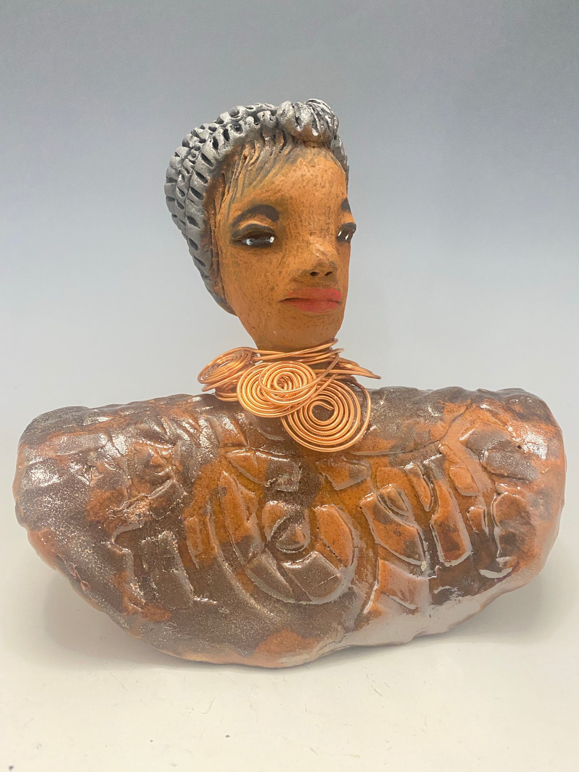 Meet Penny! Penny stands 8" x  8" x 3" and weighs 2.06 lbs. She has a lovely honey brown complexion. Penny has a metallic copper penny glaze on her textured robe. Her black eye shadow matches the black strands of baby hair around her edges. Penny's necklace has over 8 feetof spiral copper wire hair. Helen is somewhat angelic! Give Penny a porminent place in your home!