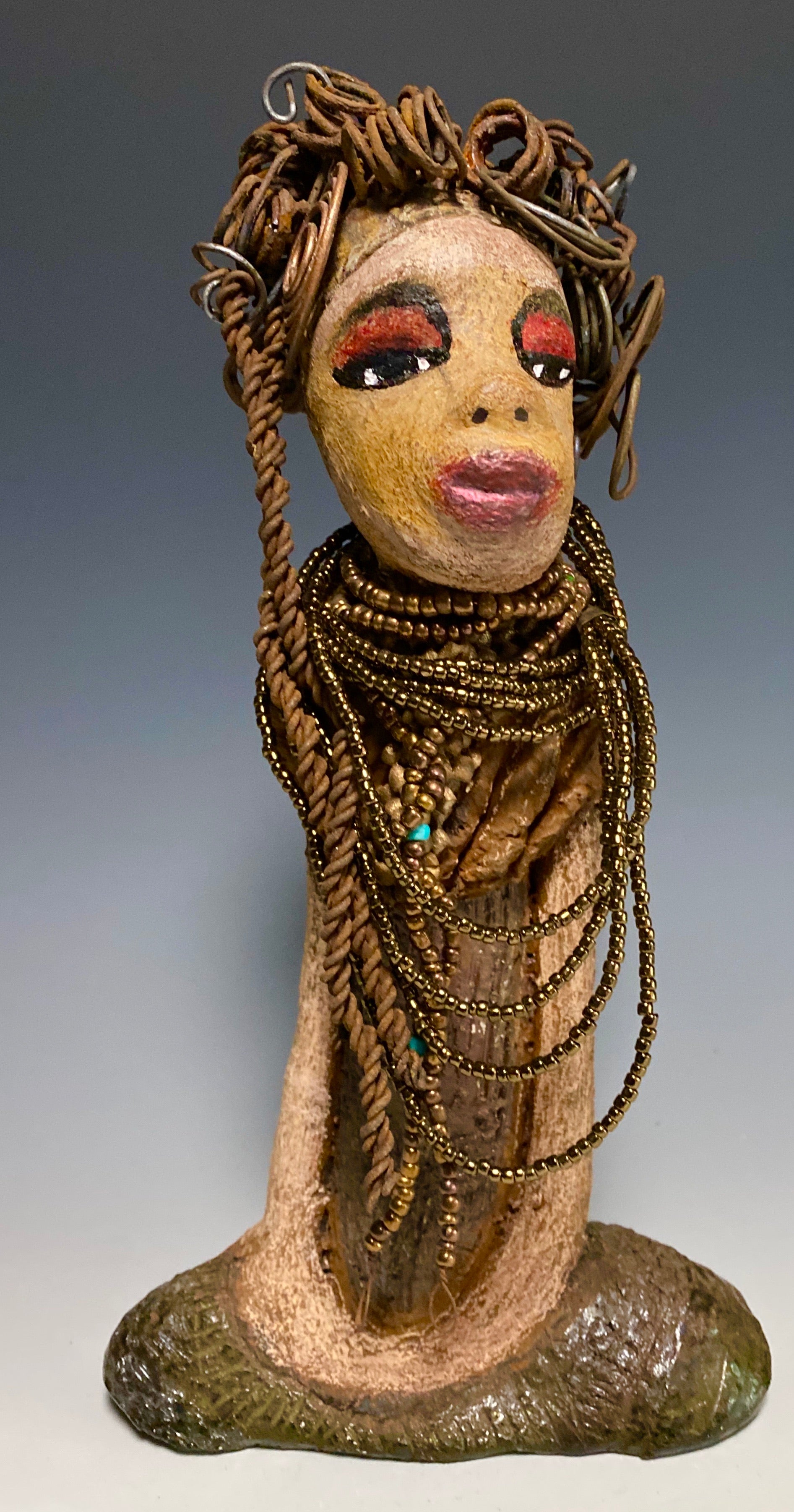 You will love having Cardi around! Cardi stands 11" x 5.5" x 3" and weighs 1.14 lbs. She has an awesome honey beige complexion. Cardi wears a dark metallic copper dress with a chocolate ruffle scarf.  She wears a multitude of amber colored hand strung beads. I do believe Cardi would like it if you gave her a space in your home!
