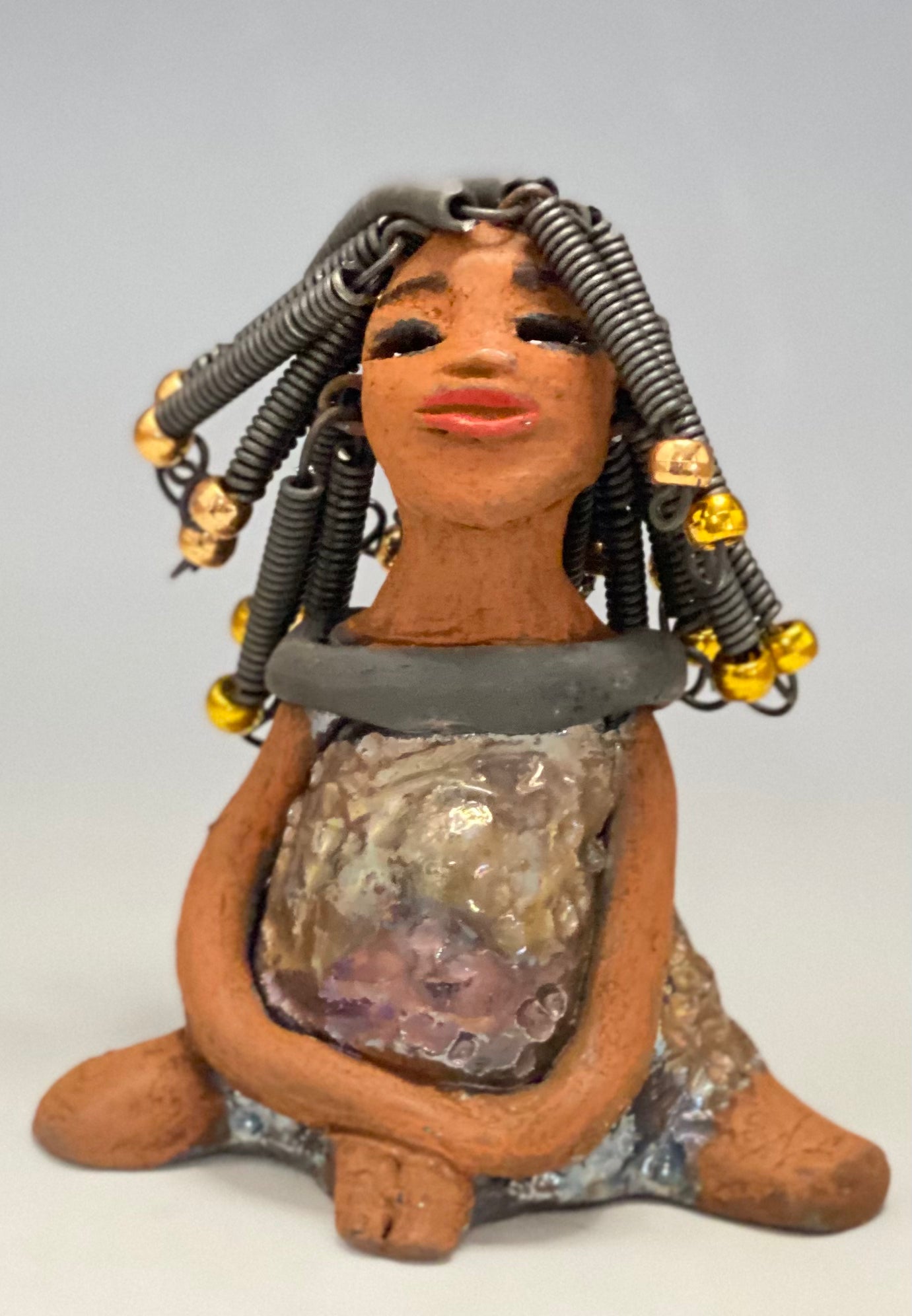 Meet Sadie Sadie stands 5.5" x 4" x 3" and weighs 8.7 ozs. She wears a lovely glossy metallic gold dress.. Sadie has over15 feet of coiled wire hair. Sadie appears to sit in a yoga pose. Her long arms rest at her side. Sadie is a great starter piece from the Herdew Collection!