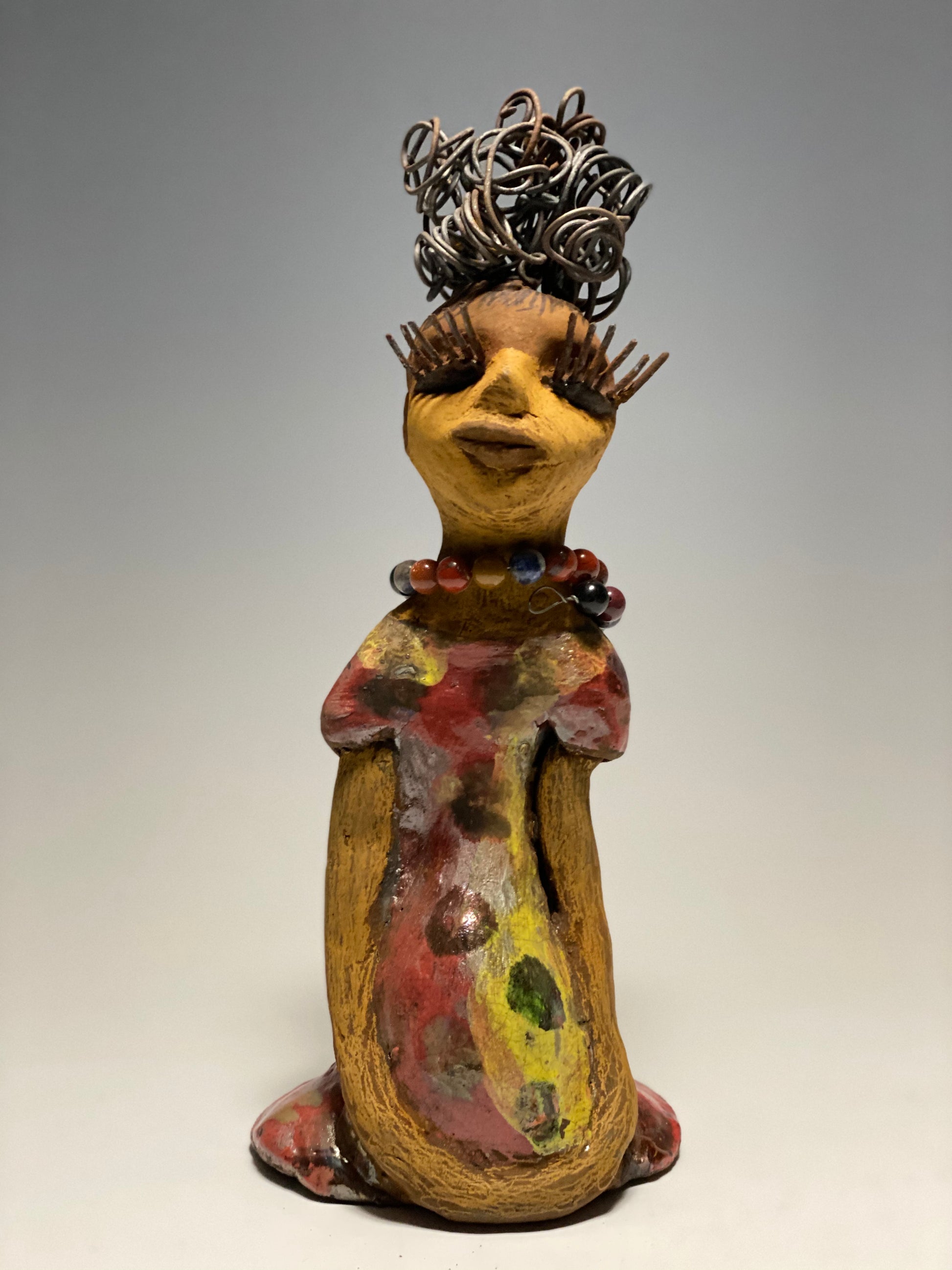 You know someone like Tiffanie. One who reaps elegance and sophistication!  Tiffanie stands 9”x 4" x 4" and weighs 1.03 lbs.  She has a two tone light beige complexion with 2 feet of 16 gauge spiral coiled wire hair.  Tiffanie metallic copper red and yellow  dress is accented by a multicolored beaded necklace. Tiffanie’s long lashes and  black eye shadow gives her a distinguished mystical look.